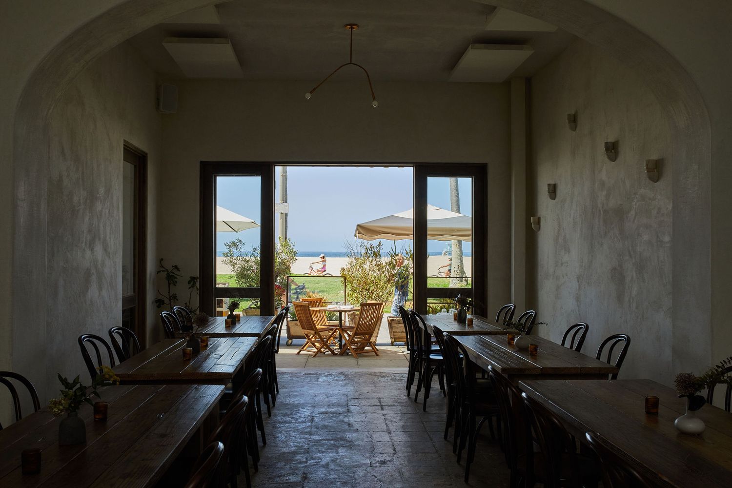 Restaurant interior with wooden tables leading to window view of ocean.