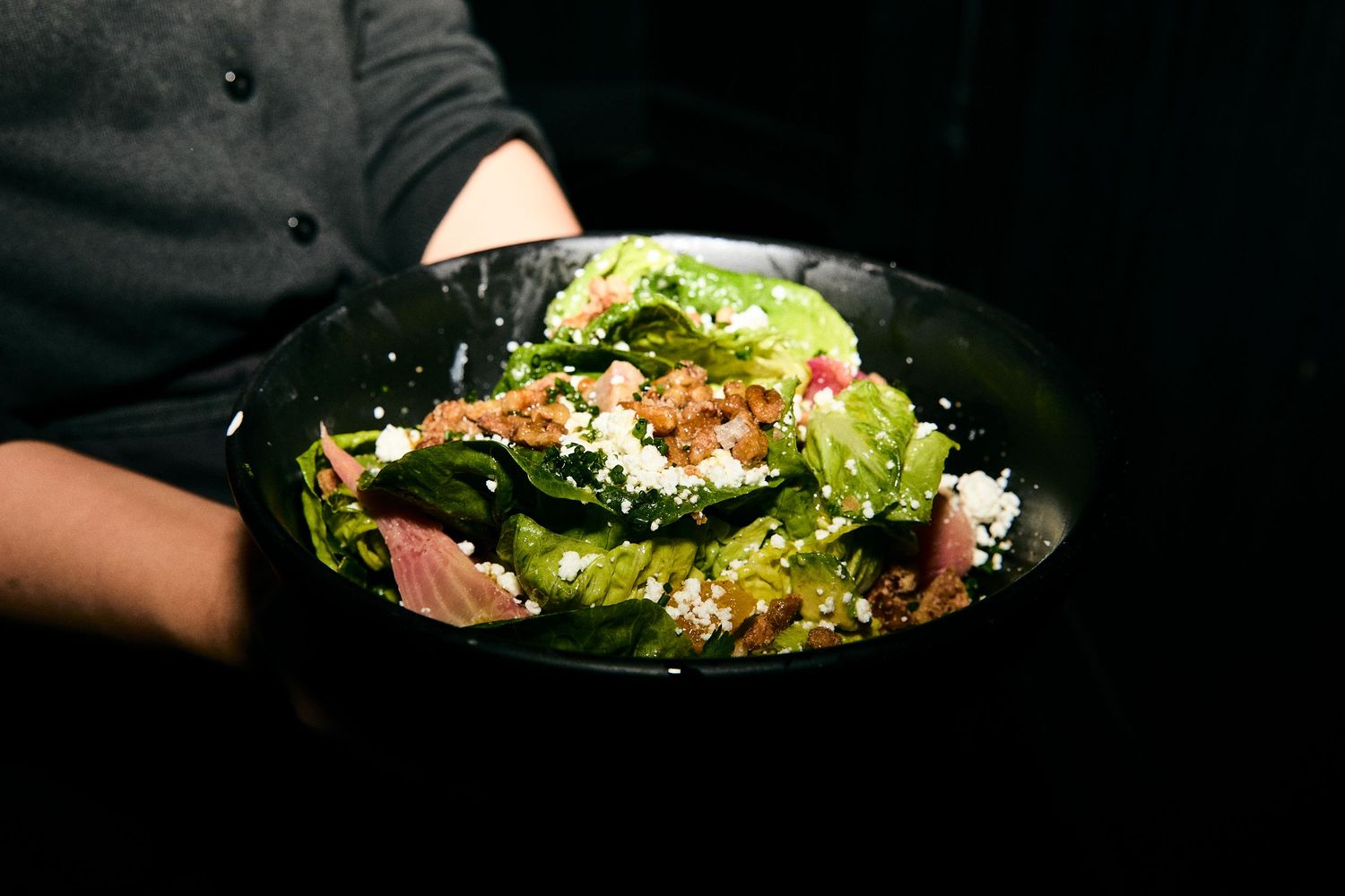 Bowl of fresh green salad with colorful toppings and garnishes served on dark surface with dramatic lighting.