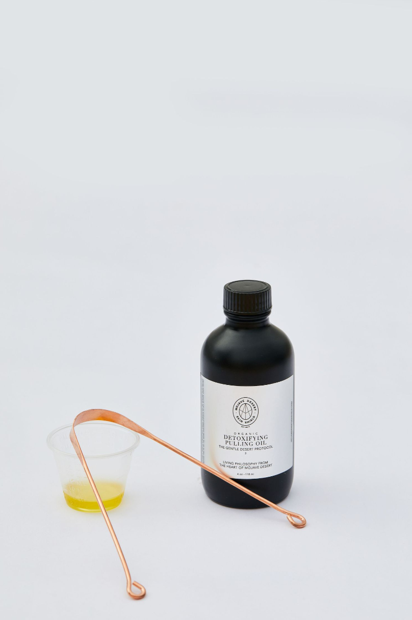 Black bottle with minimalist label and copper tongue cleaner against white background.
