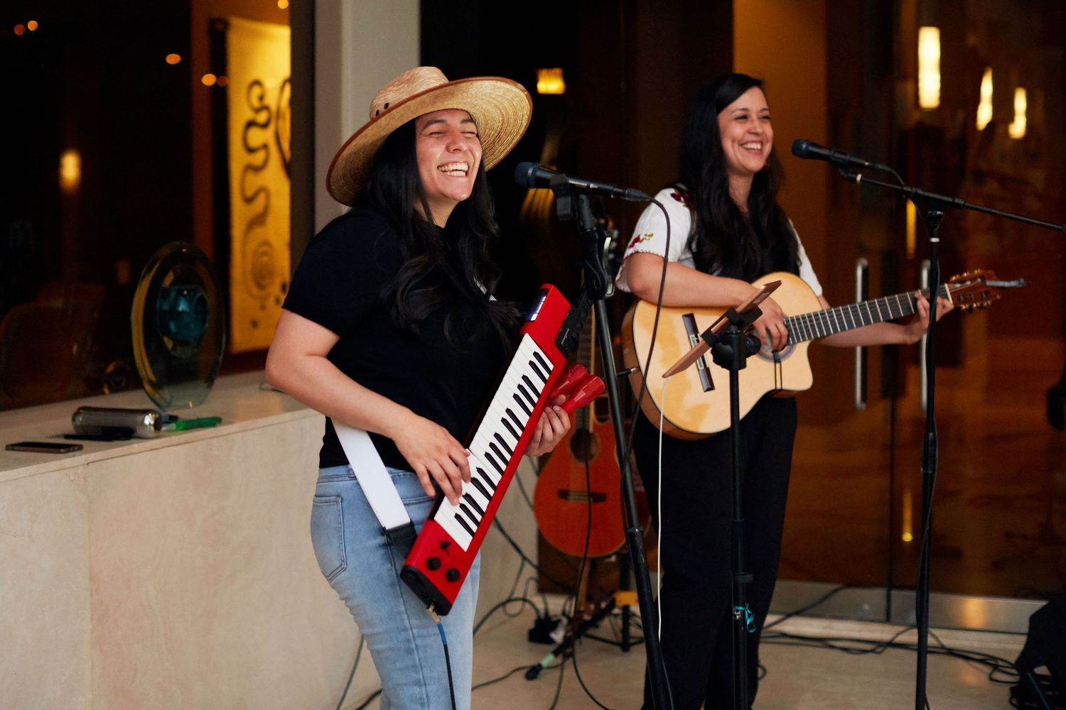 Musicians perform on stage with one playing a keytar and one playing acoustic guitar at an indoor venue.