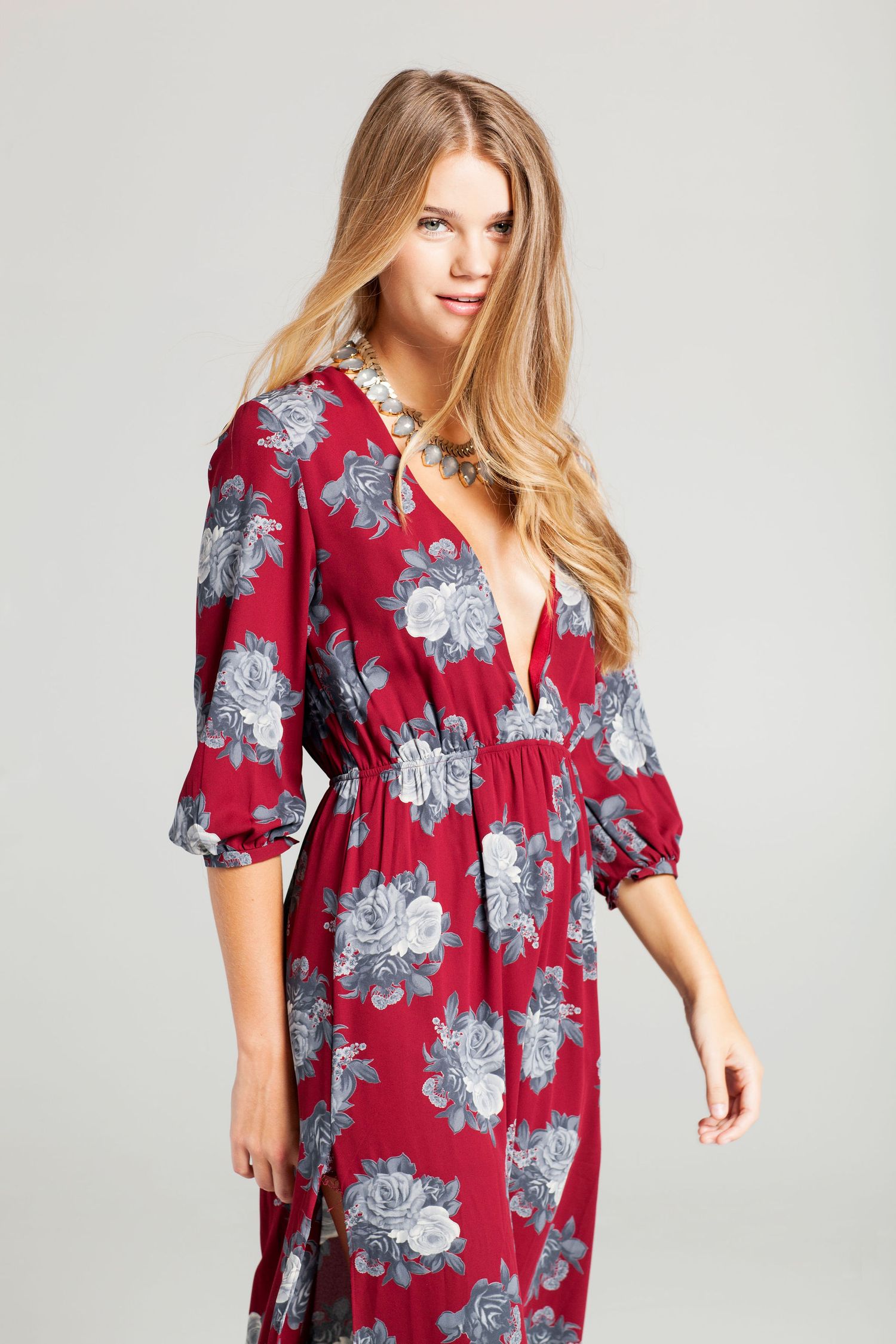 Fashion model wearing red floral print dress with three-quarter length sleeves against grey background.