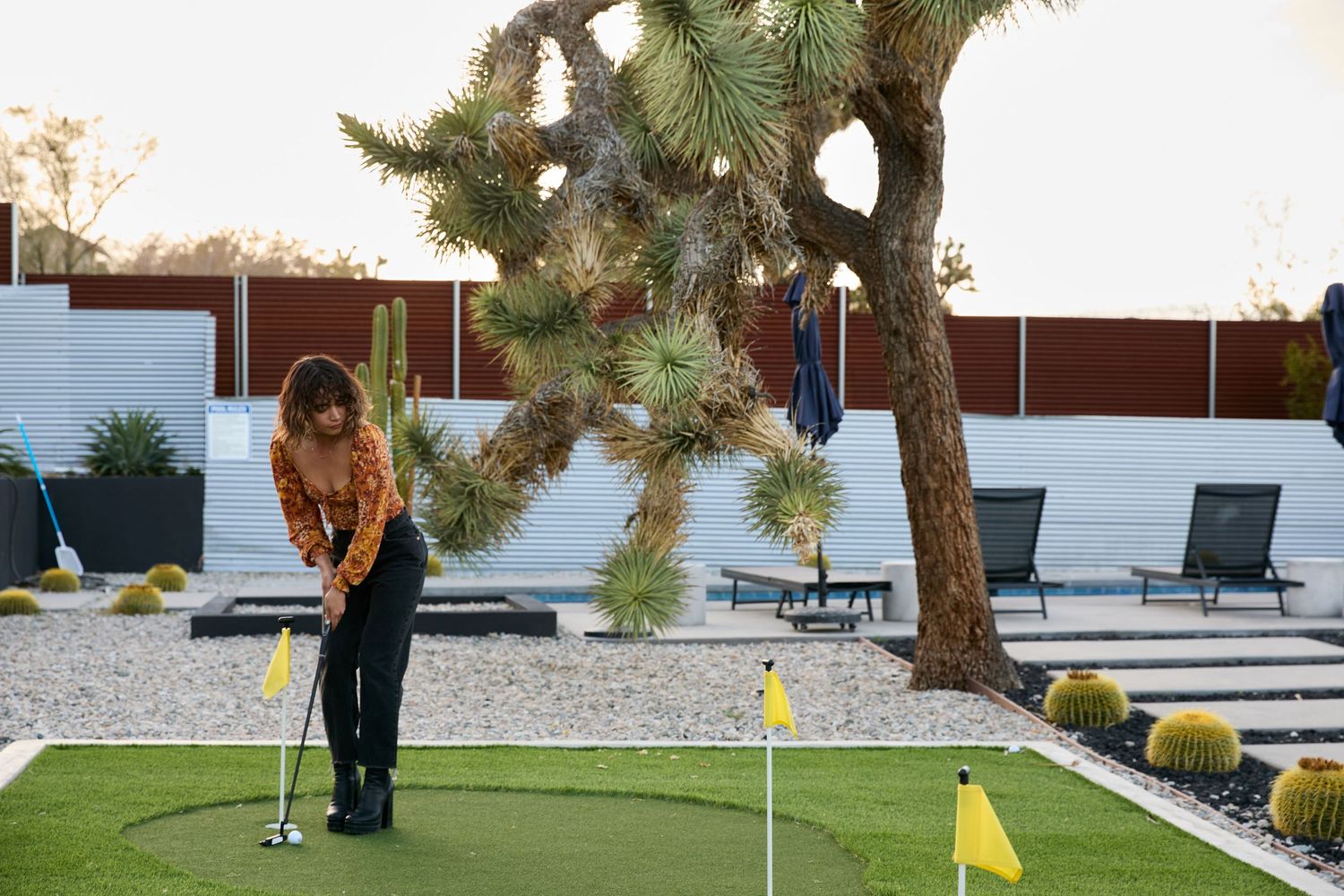 Woman practicing putting on a backyard mini golf green surrounded by Joshua trees and desert landscaping.