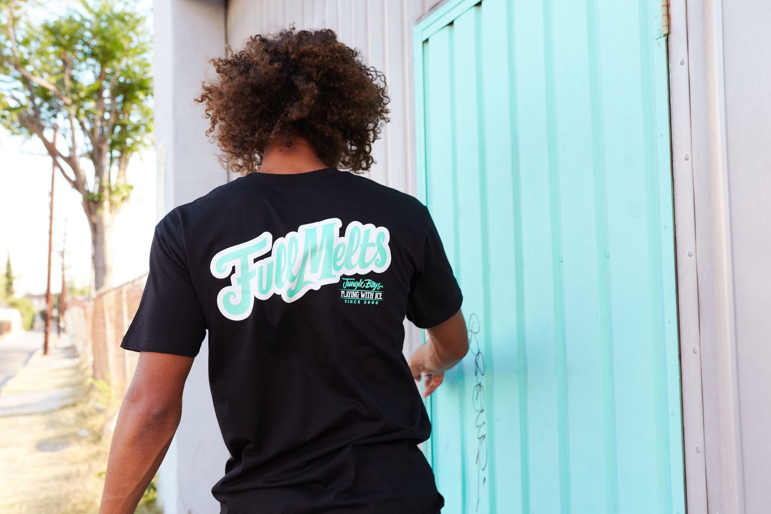 Back view of person wearing black t-shirt with retro graphics near turquoise wall.
