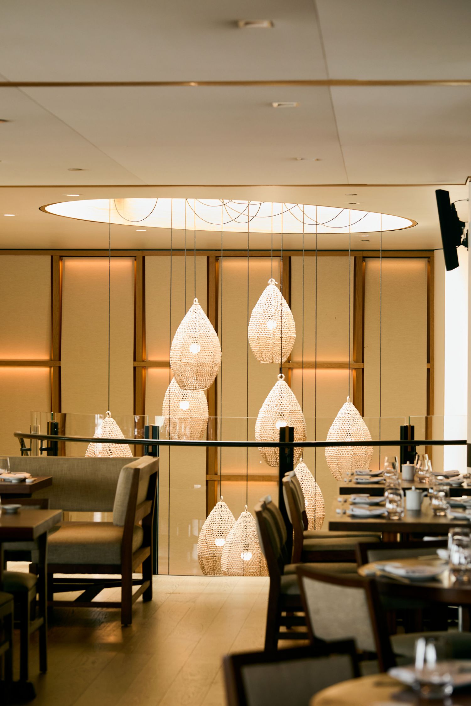 Elegant white lace-style pendant lights hang from a skylight in an upscale restaurant dining room with plush seating.