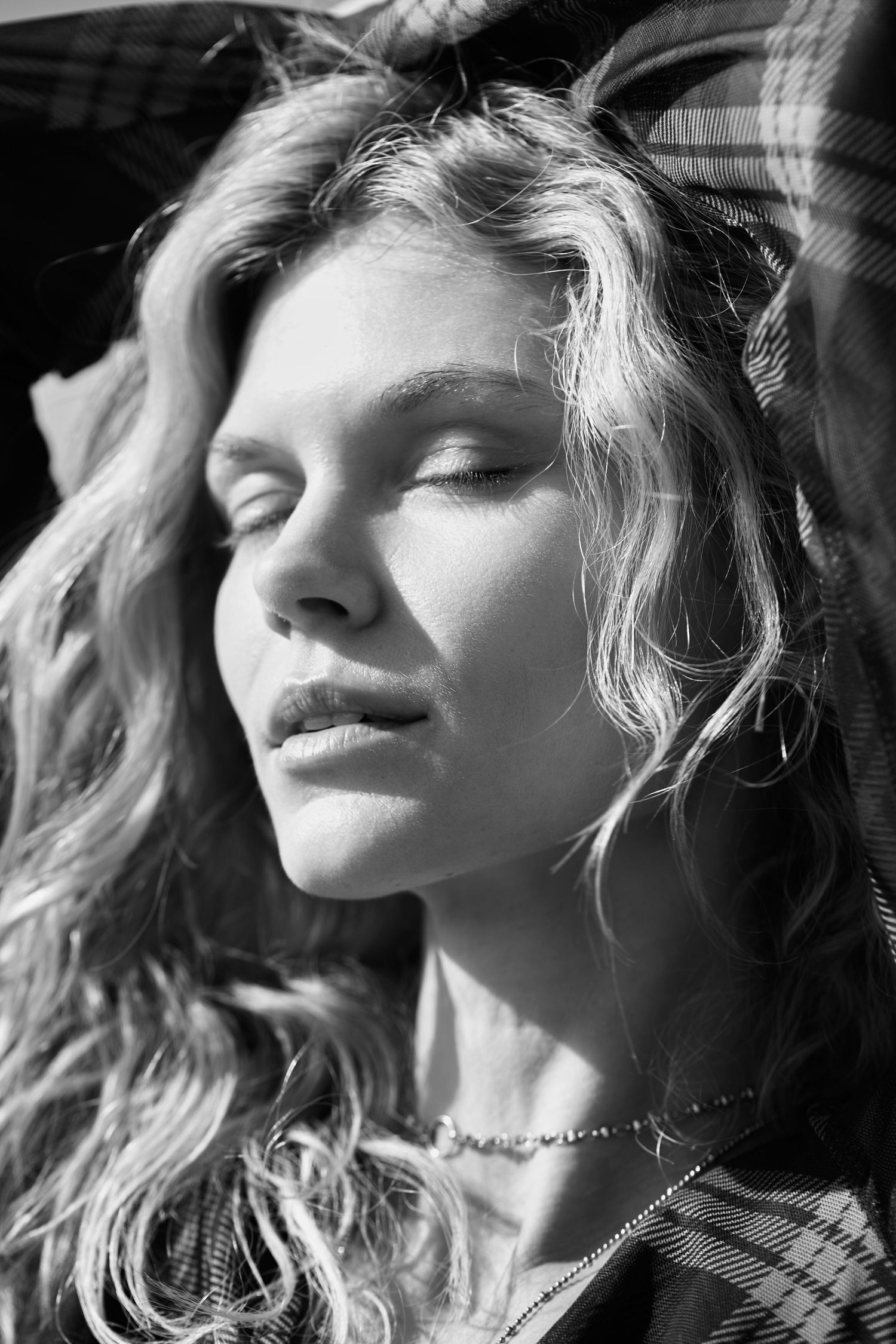 Black and white portrait of a person with wavy blonde hair in dramatic sunlight with closed eyes.