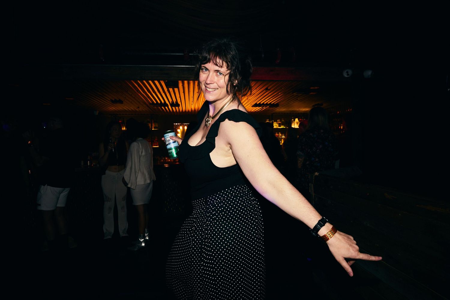 A performer dances energetically in a dark nightclub setting illuminated by colorful spotlights.