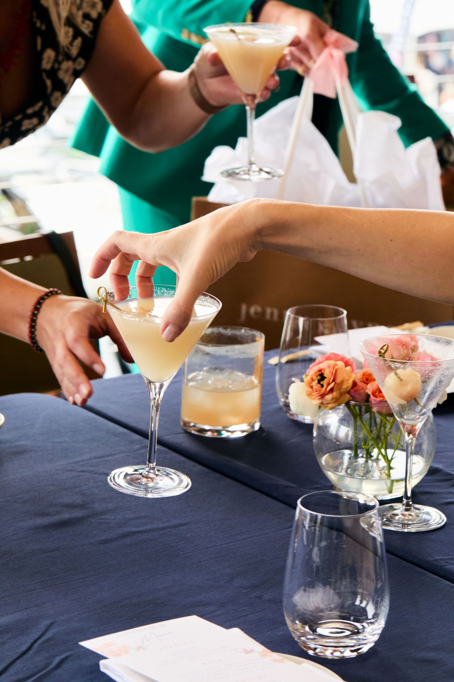 Champagne cocktails being served on a navy blue tablecloth with delicate pink flowers in a small vase.