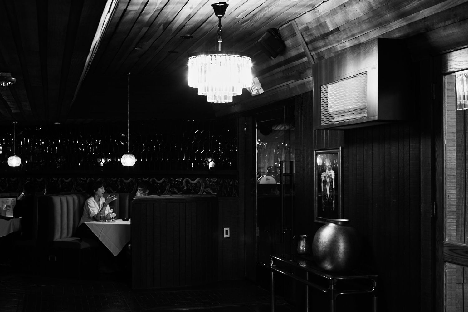A dimly lit bar interior with art deco chandeliers and wood paneling creates a moody vintage atmosphere.