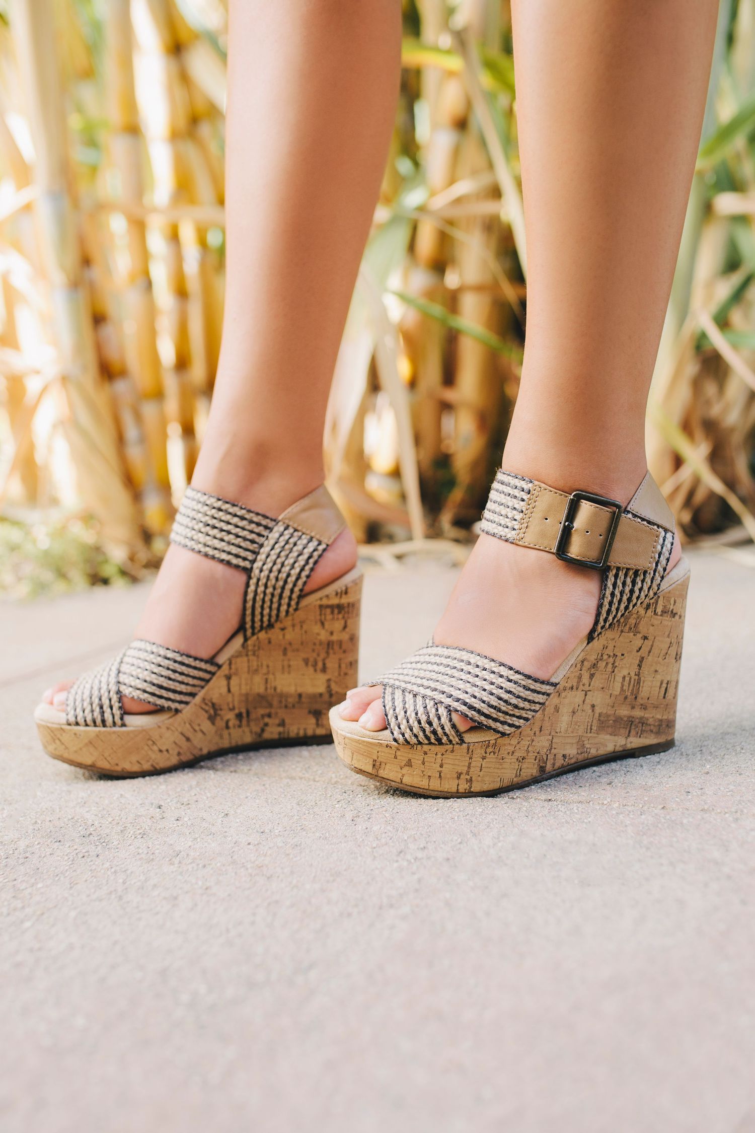 Woman wearing beige woven strap cork wedge sandals with decorative striped pattern and ankle buckle closure.