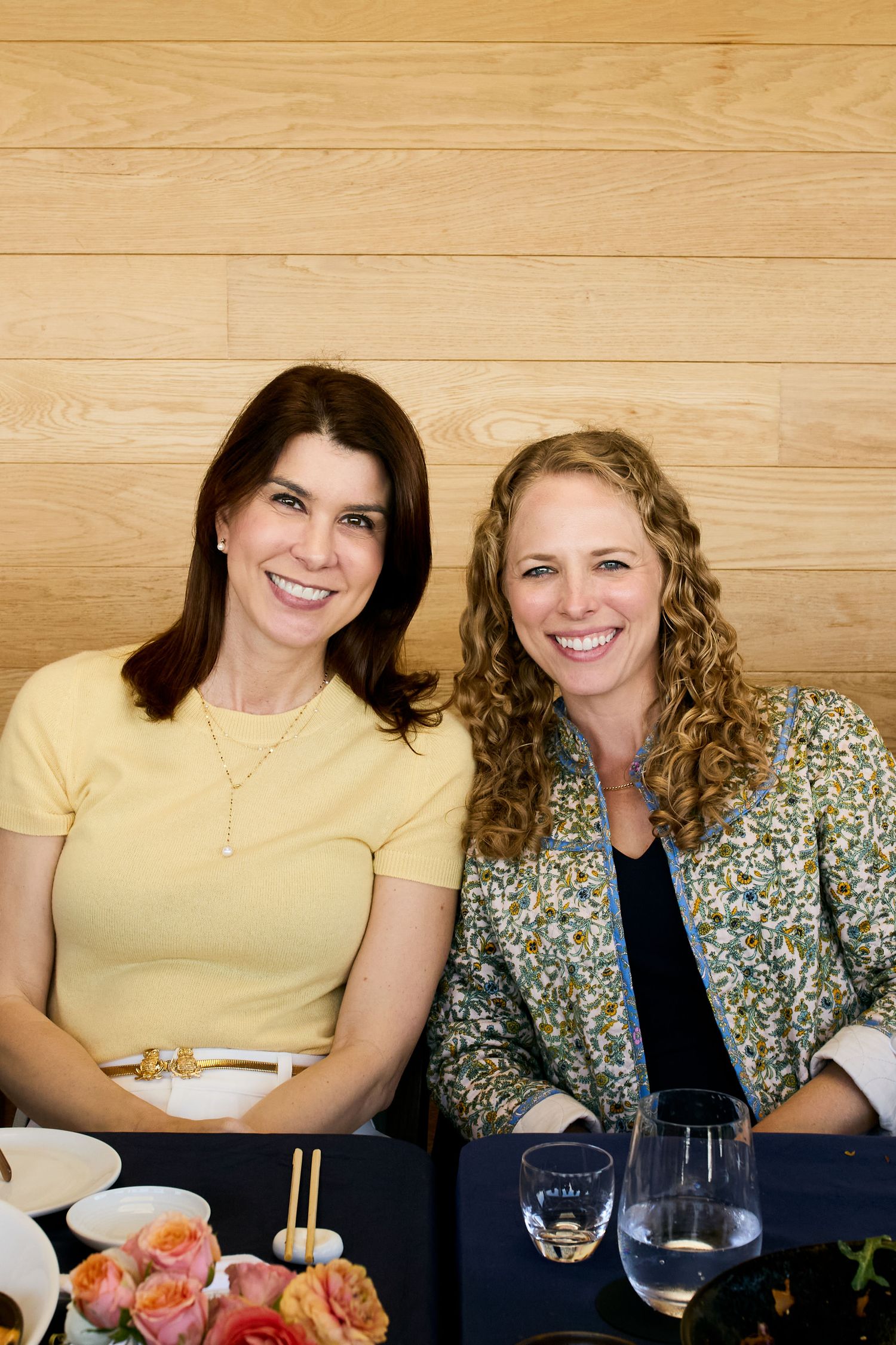 Two friends enjoying sushi and wine at a table against a wooden wall backdrop.