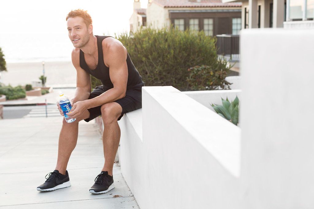 Athletic person in sportswear taking a break while sitting on white ledge outdoors with water bottle.