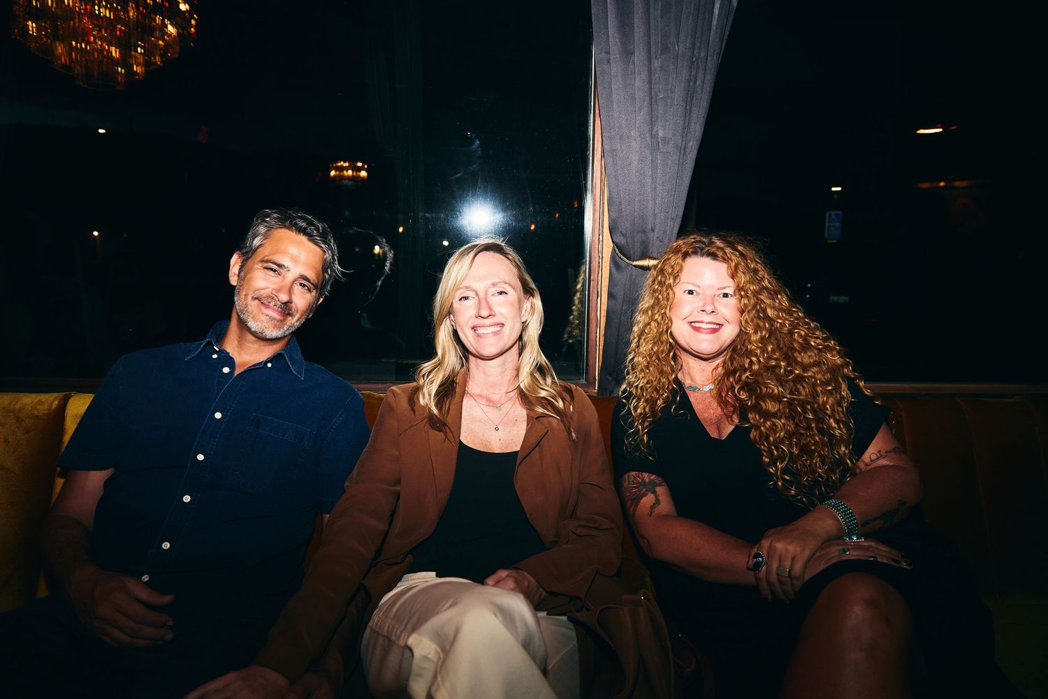 Three friends sit together at night sharing a laugh outdoors with warm lighting and smiles.