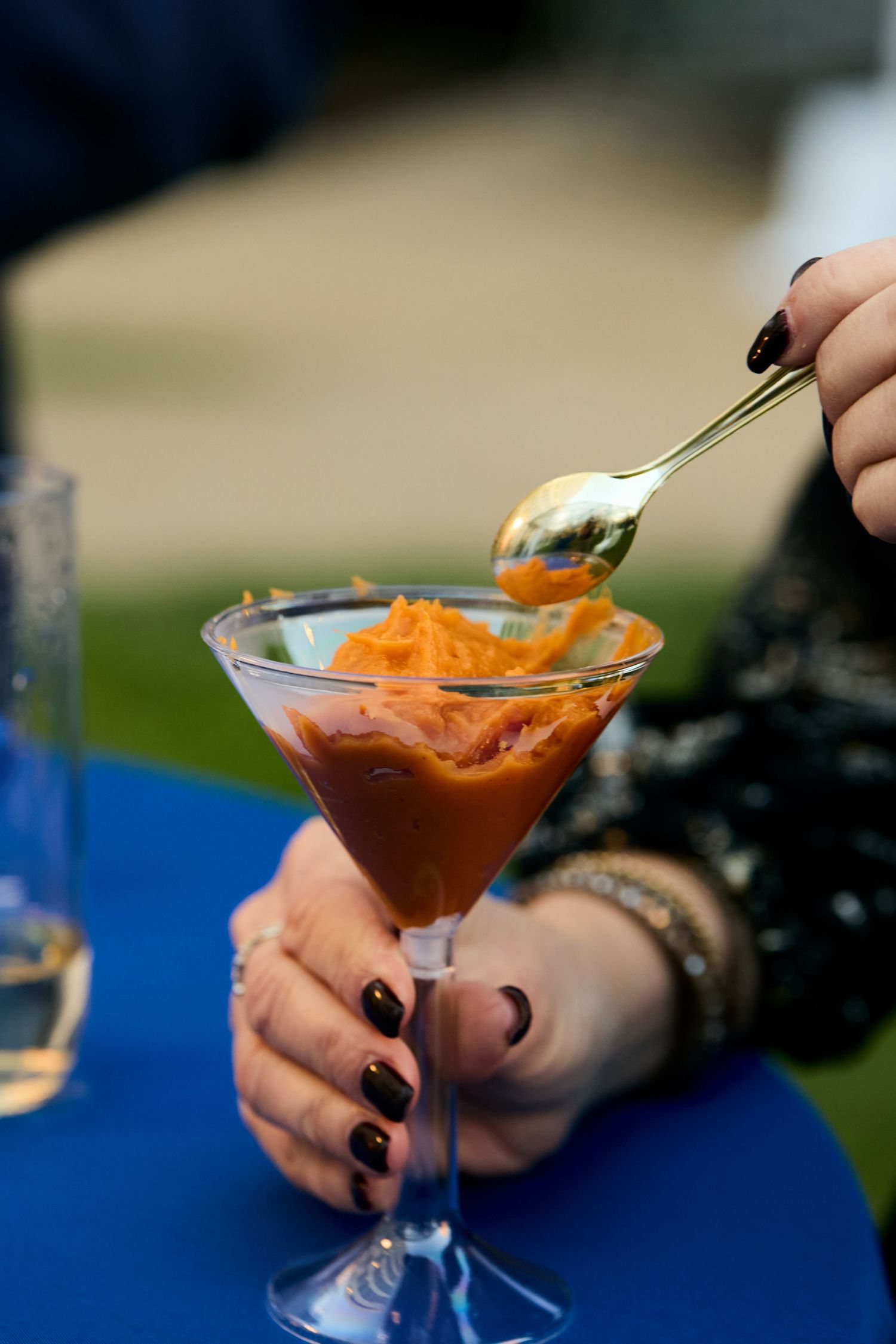 A series of martini glasses filled with orange and red cocktails being garnished with fresh herbs on a blue surface.