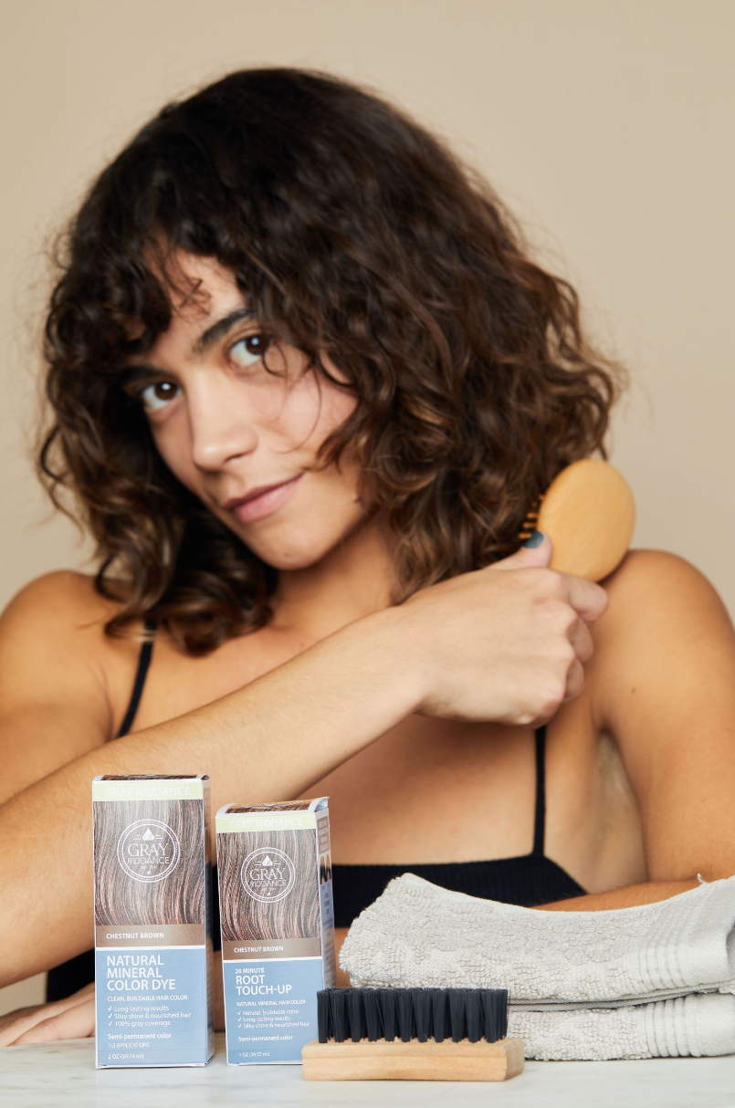 Beauty product flatlay featuring hair care items and wooden brush against neutral backdrop.