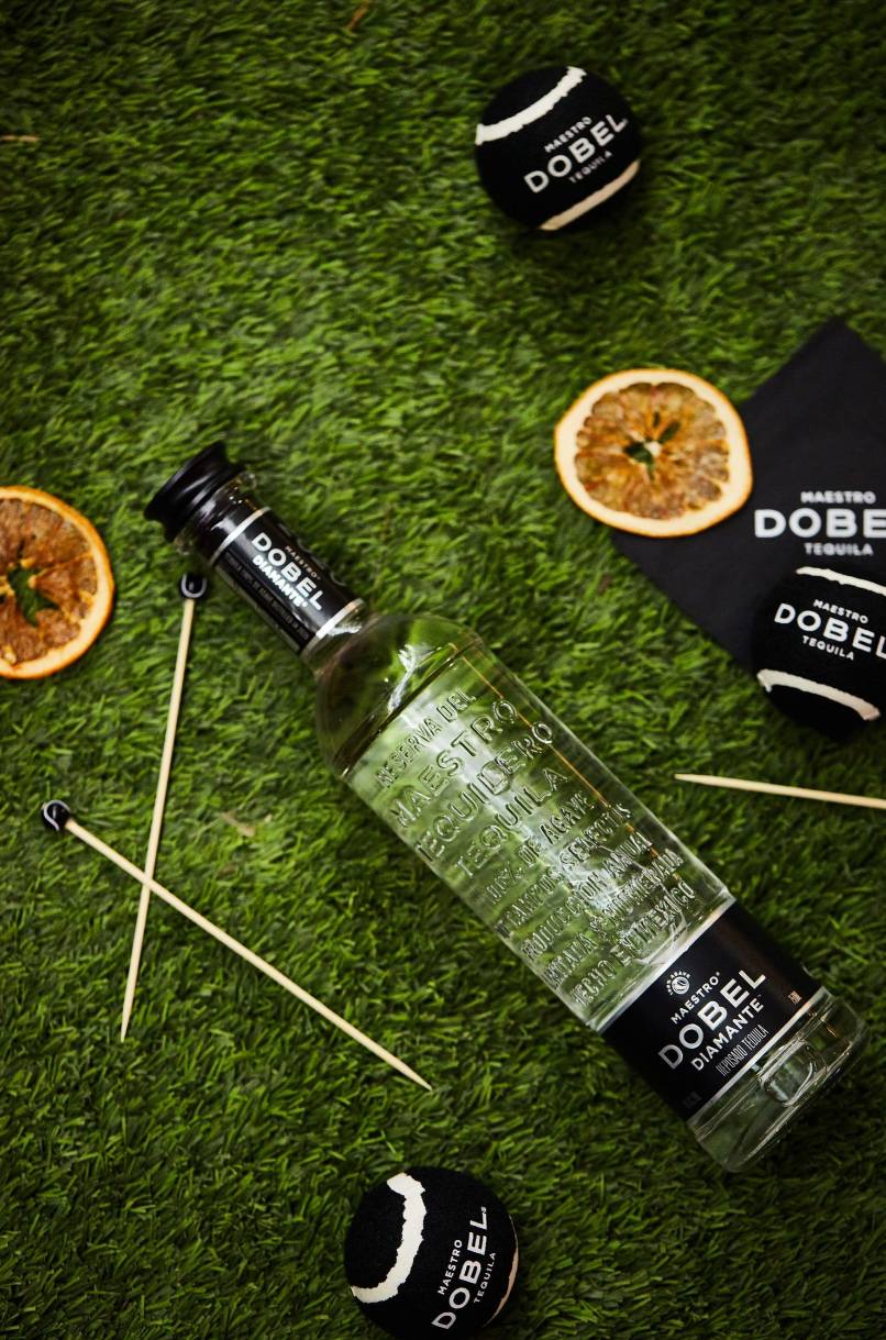 Glass bottle and citrus decorations arranged on artificial grass with branded black bottle caps.