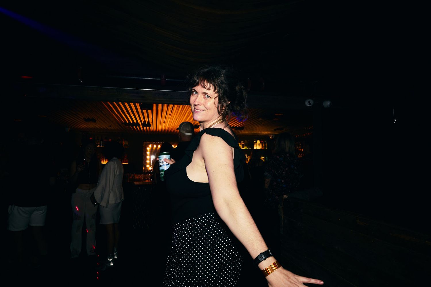 A dancer in a black polka dot dress moves on a dark dance floor with glowing lights in the background.