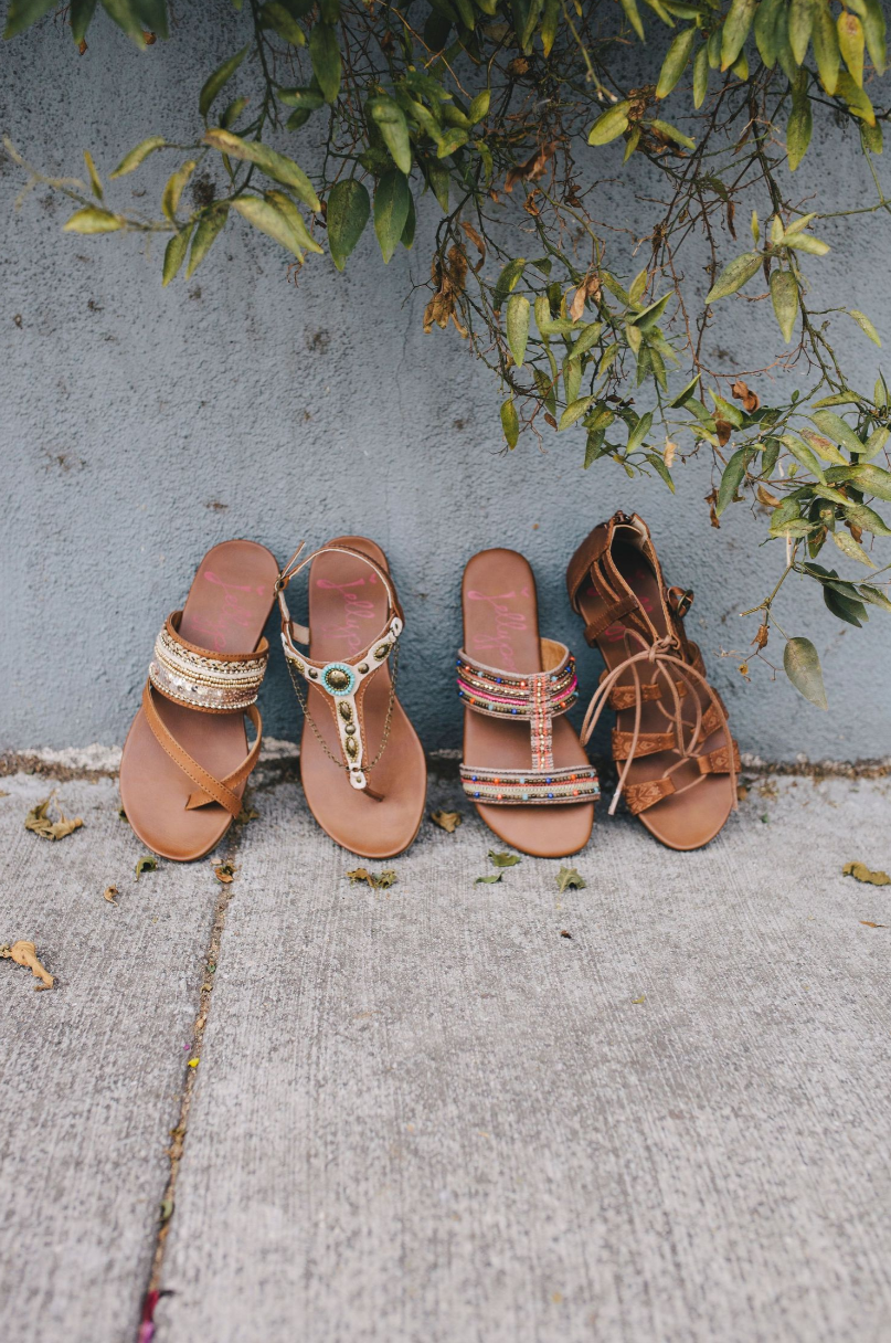 Four brown leather sandals lined up against concrete wall with hanging green foliage.