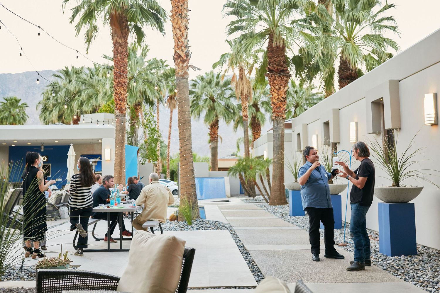 Event guests mingle in an outdoor courtyard surrounded by palm trees and white buildings.