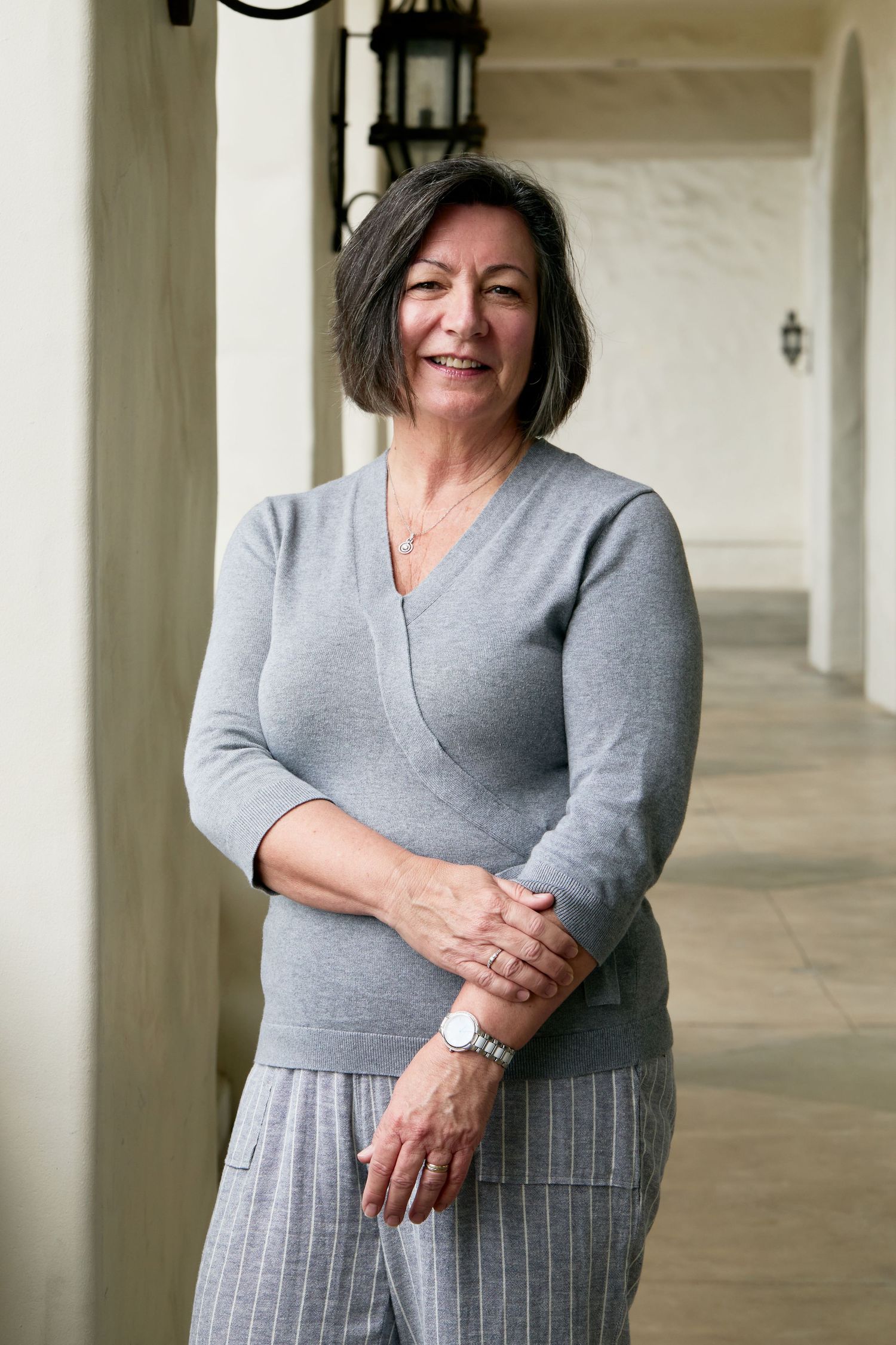 A figure in a grey wrap dress and striped skirt poses against a white colonnade in a series of casual portraits.