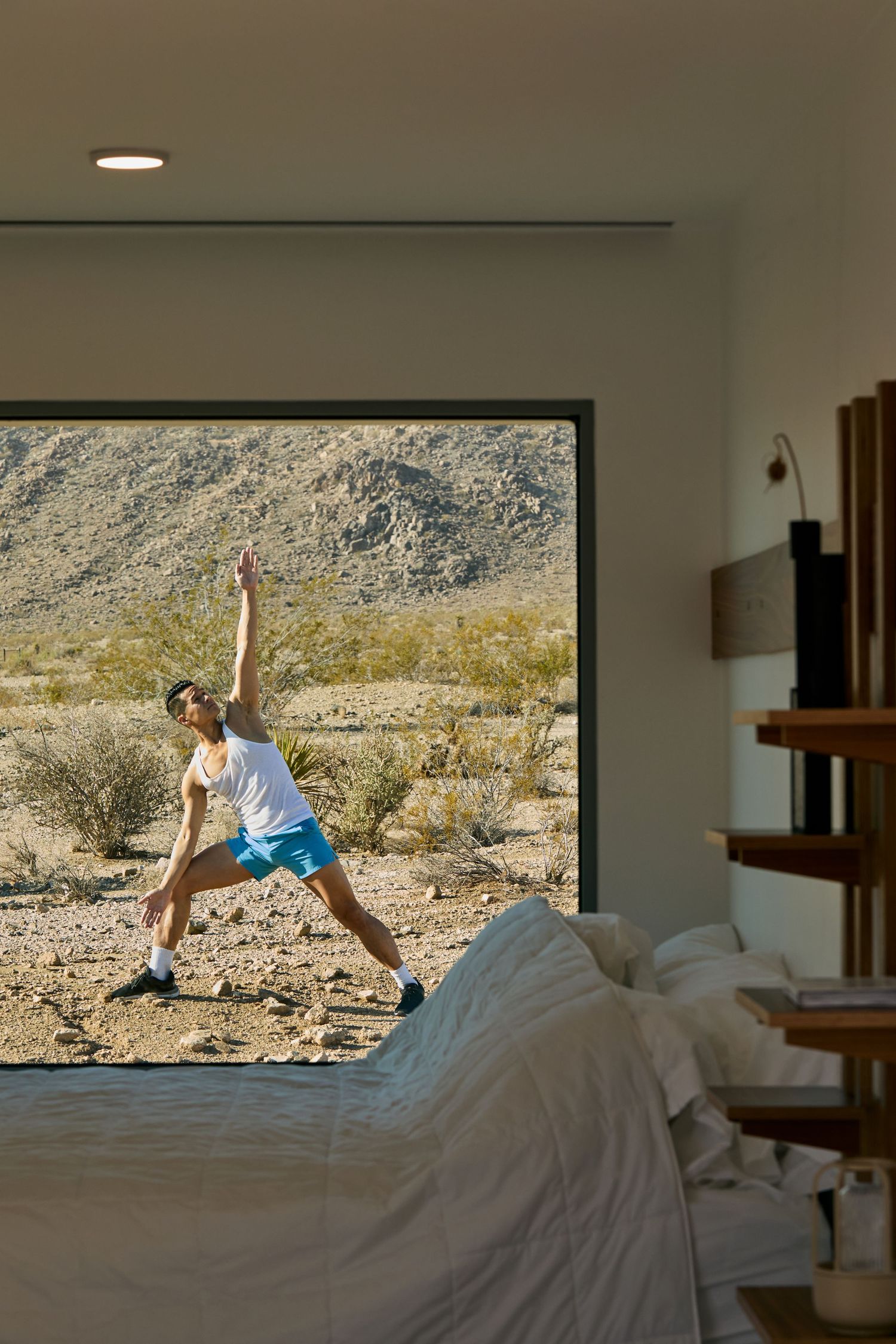Person doing yoga stretches in front of large window overlooking desert landscape with mountains and scrub brush.