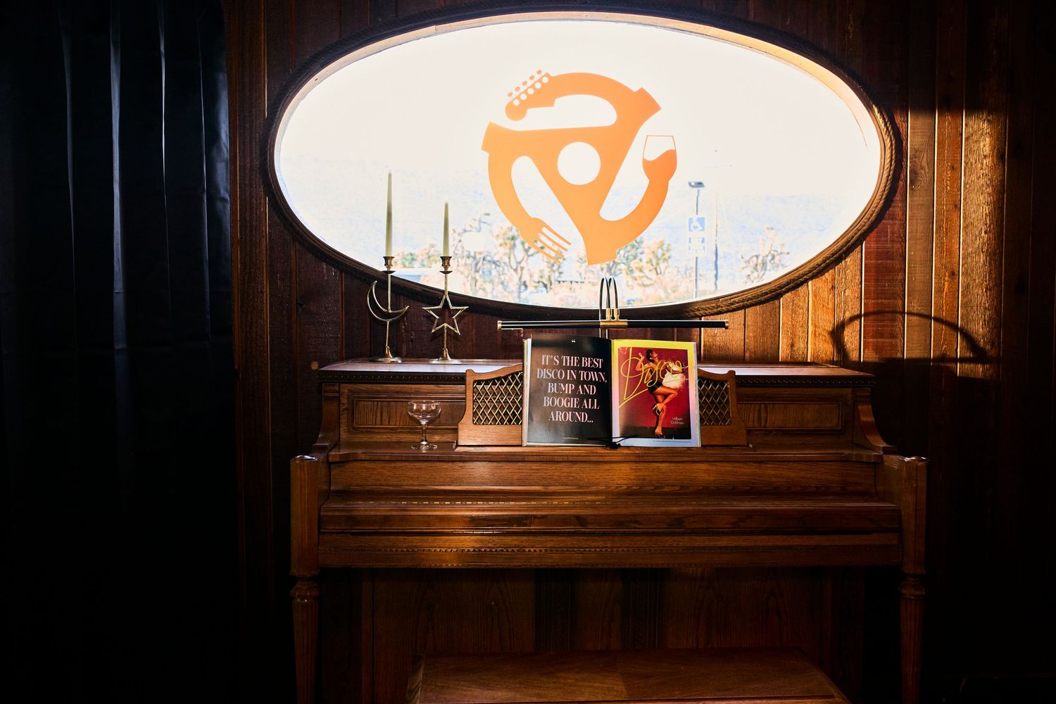 Vintage wooden piano against dark wall with illuminated orange logo sign and candlesticks on display.