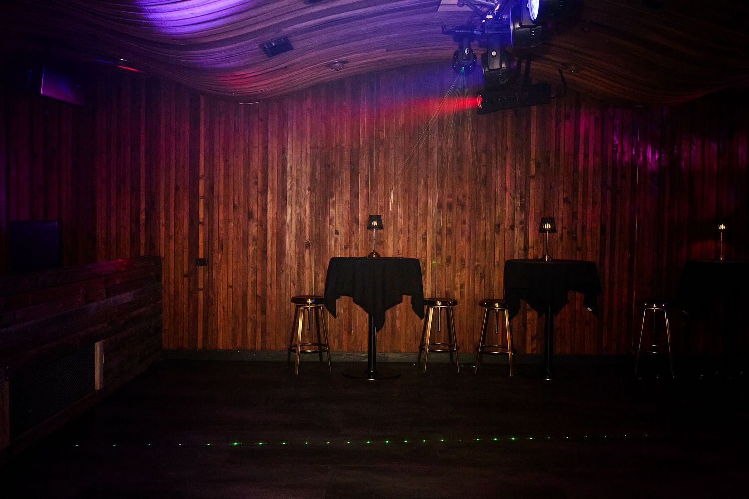 Empty stage with wooden walls, red curtains and purple lighting in a performance venue.