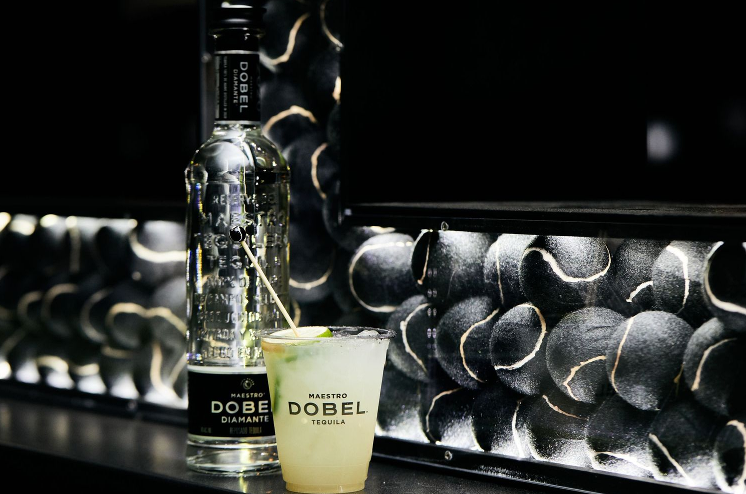 Glass bottle of Dobel tequila with cocktail on reflective black surface.