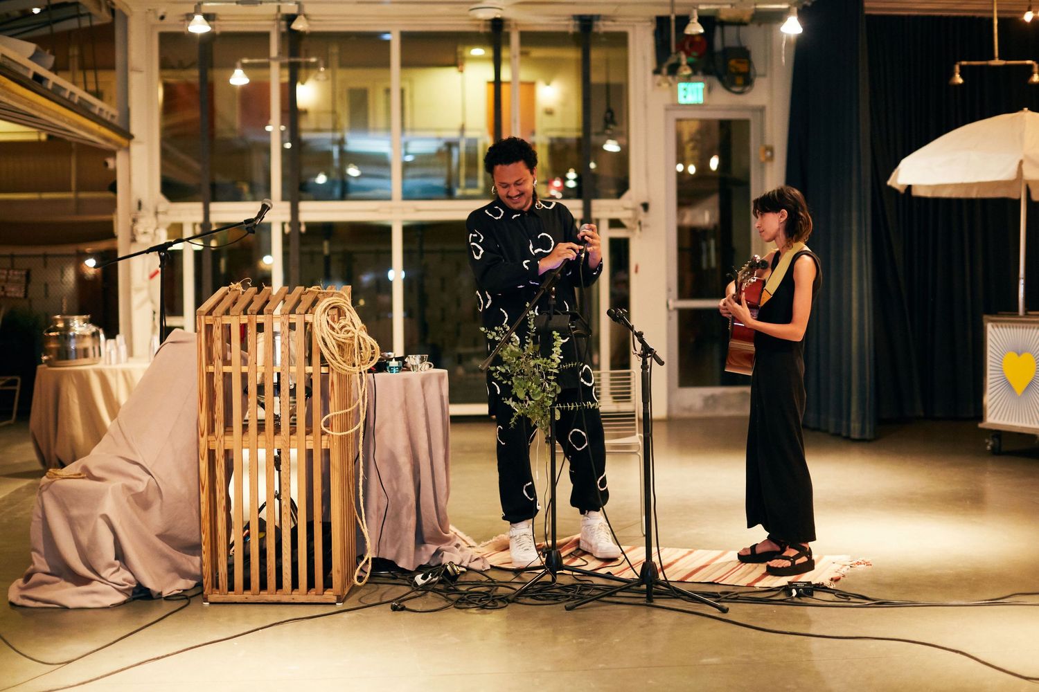 Musicians perform with instruments on a stage decorated with beige drapes and ambient lighting during an indoor event.