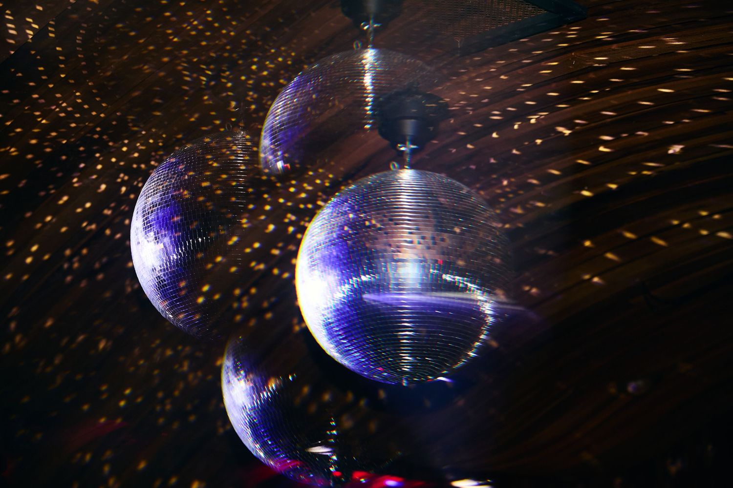 Shiny disco balls with purple and blue reflections hanging in a dark club setting with scattered light effects.