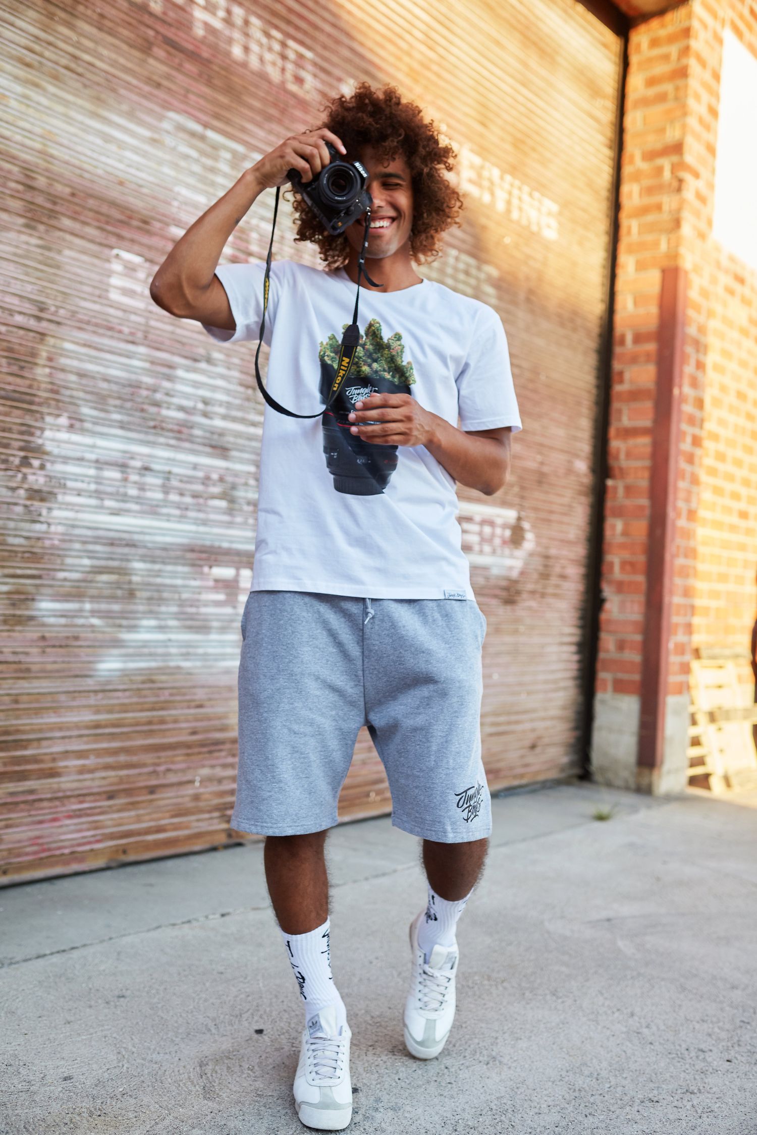 Urban photographer in casual wear holding camera and plant against brick wall background.