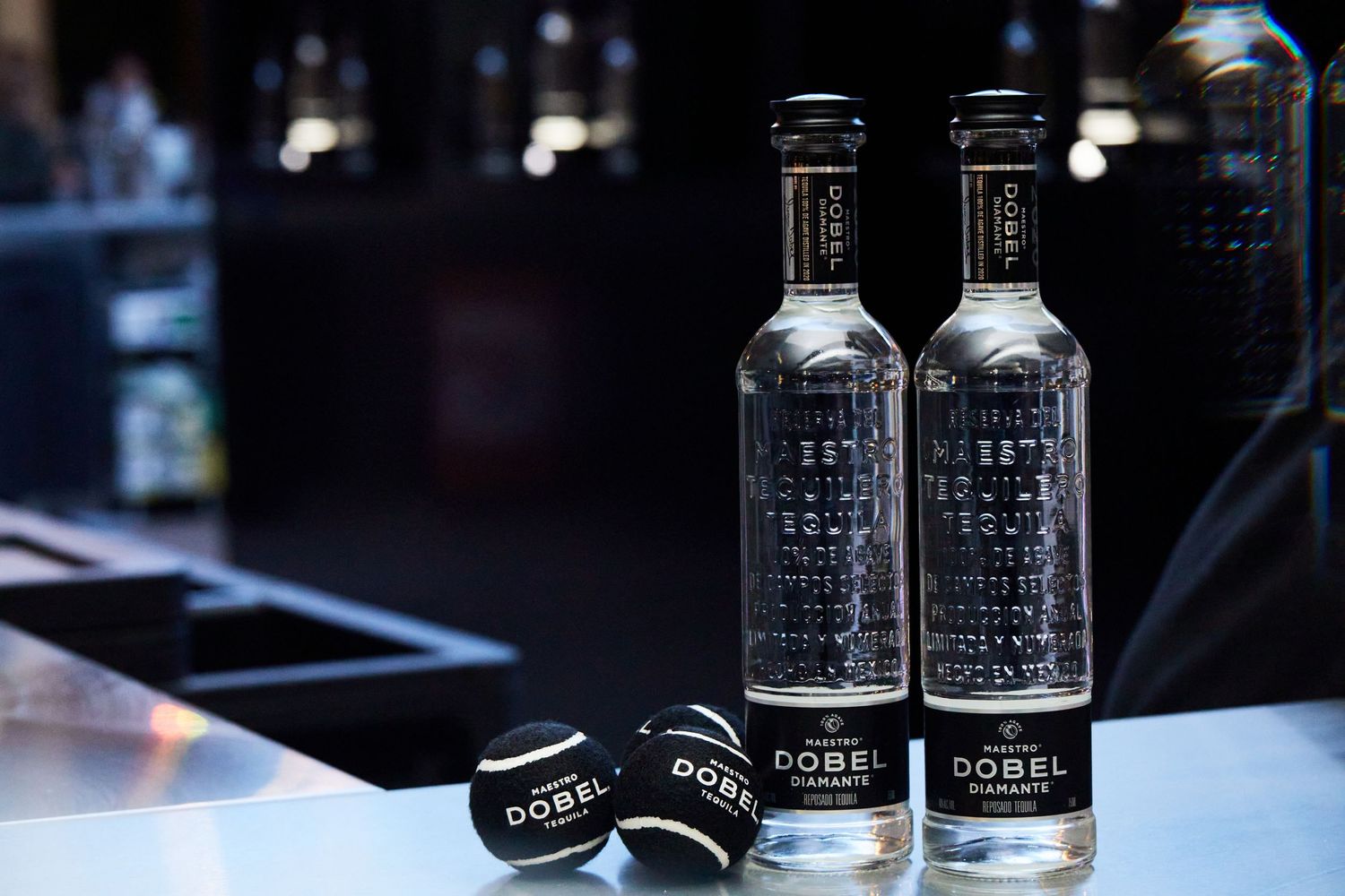 Glass bottles of premium spirits arranged with black bottle caps on dark reflective surface.