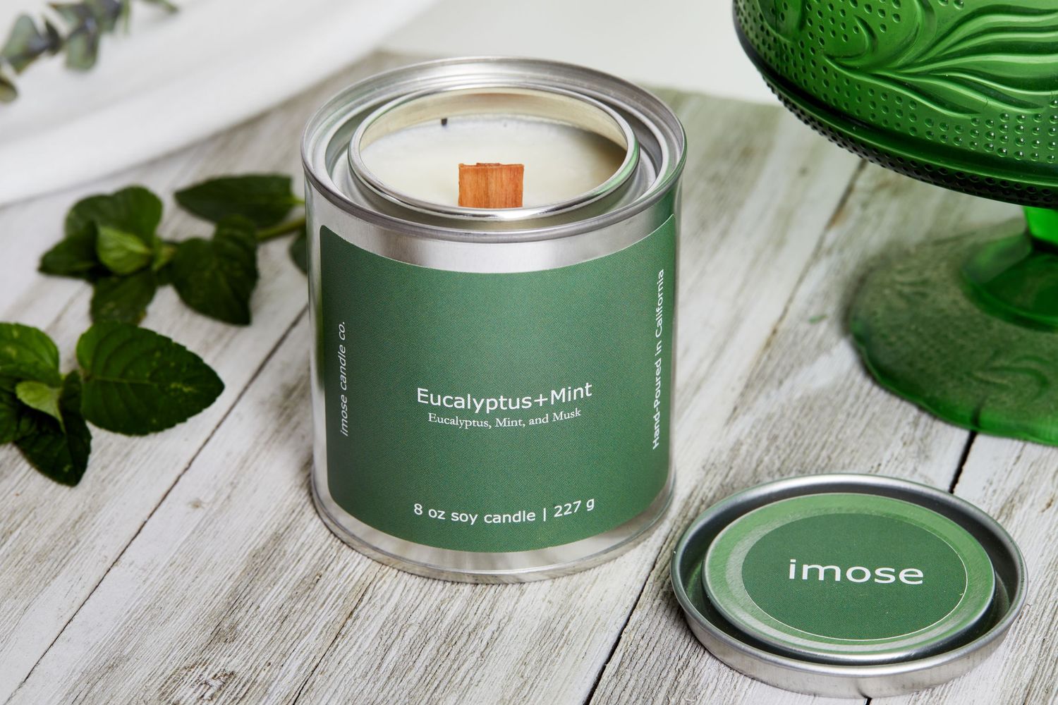 Green tin candle container with wooden wick and matching decor elements.