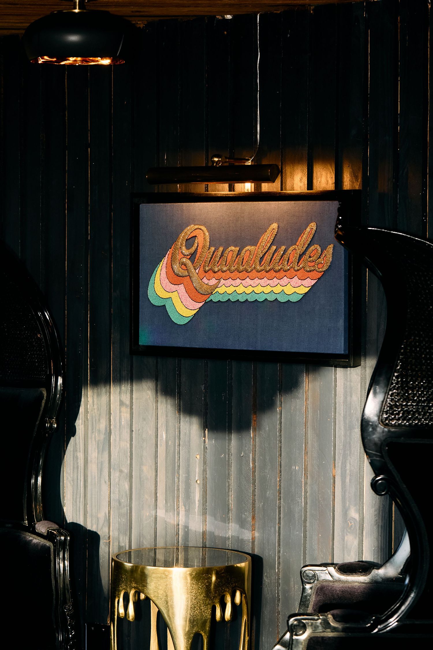 Retro rainbow-colored 'Quaaludes' neon sign mounted on a dark wooden wall with vintage decor elements.
