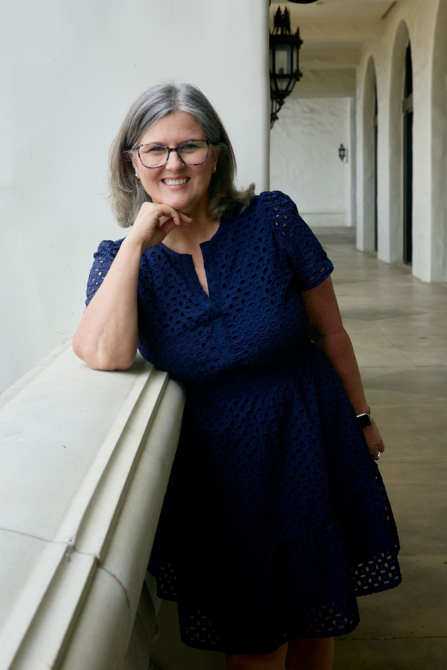 A person in a navy blue eyelet dress poses in a series of casual shots along a white columned walkway.
