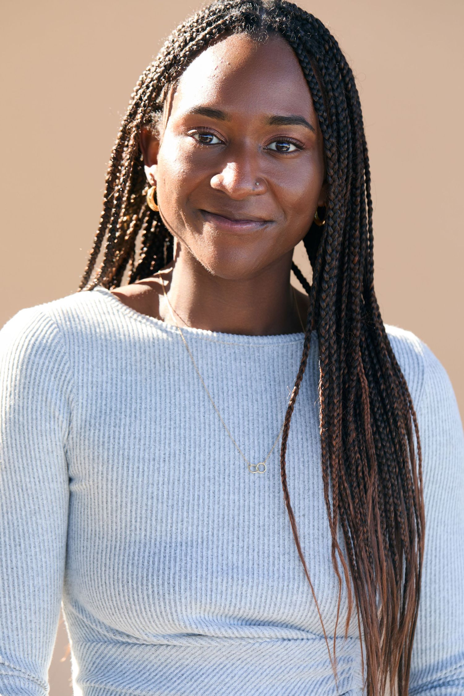 Portrait of someone with long braided hair wearing a white ribbed sweater against a neutral background.