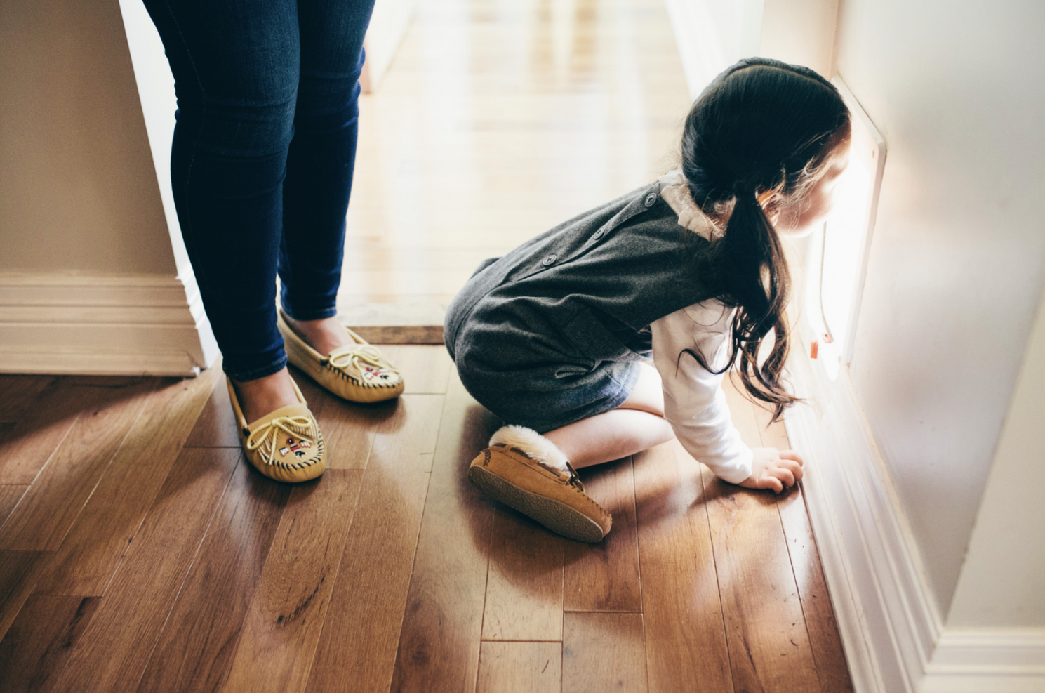 Child crawling on hardwood floor with adult feet visible in background.