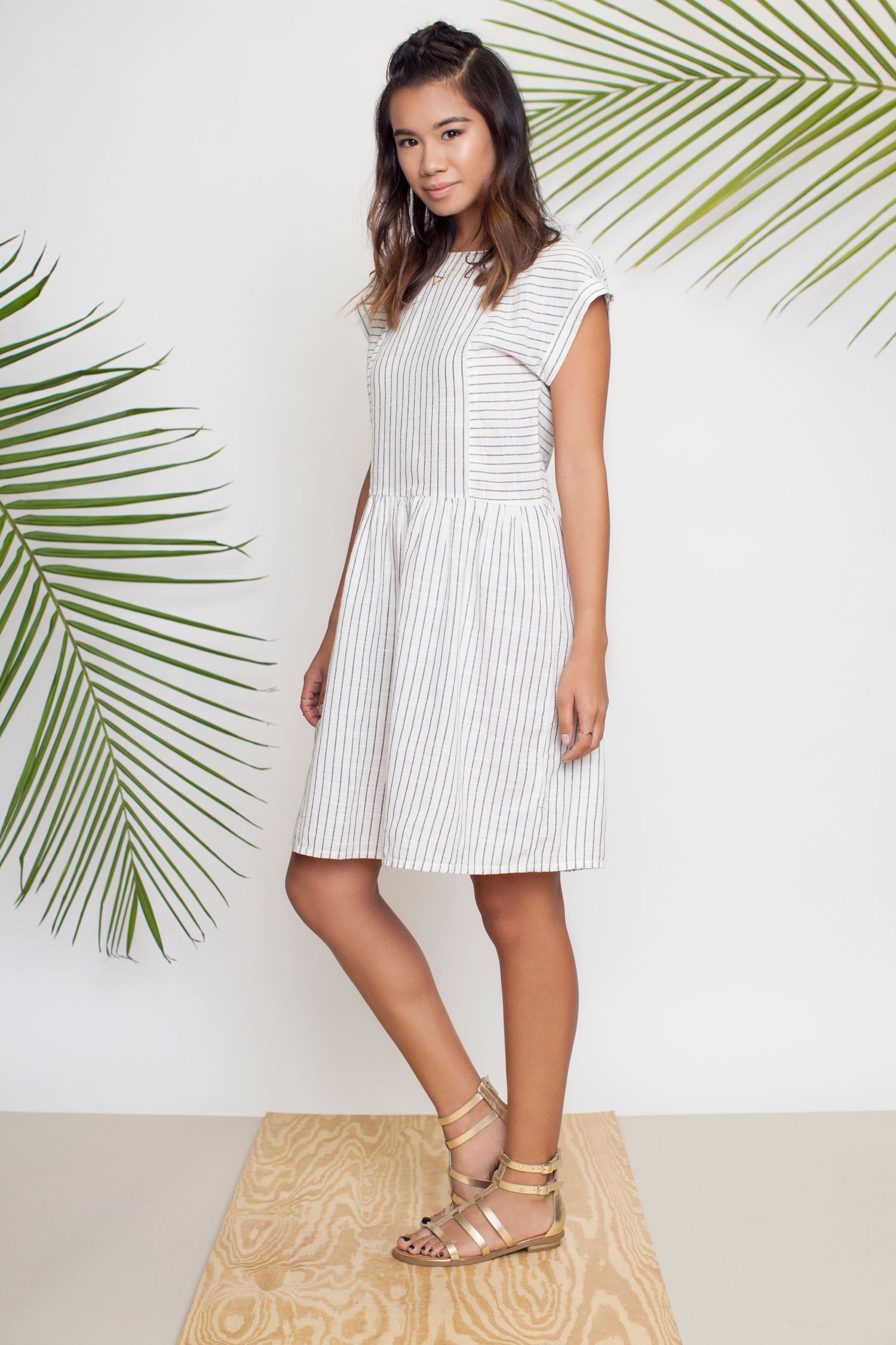 White and grey striped sleeveless midi dress styled with palm leaves in the background.