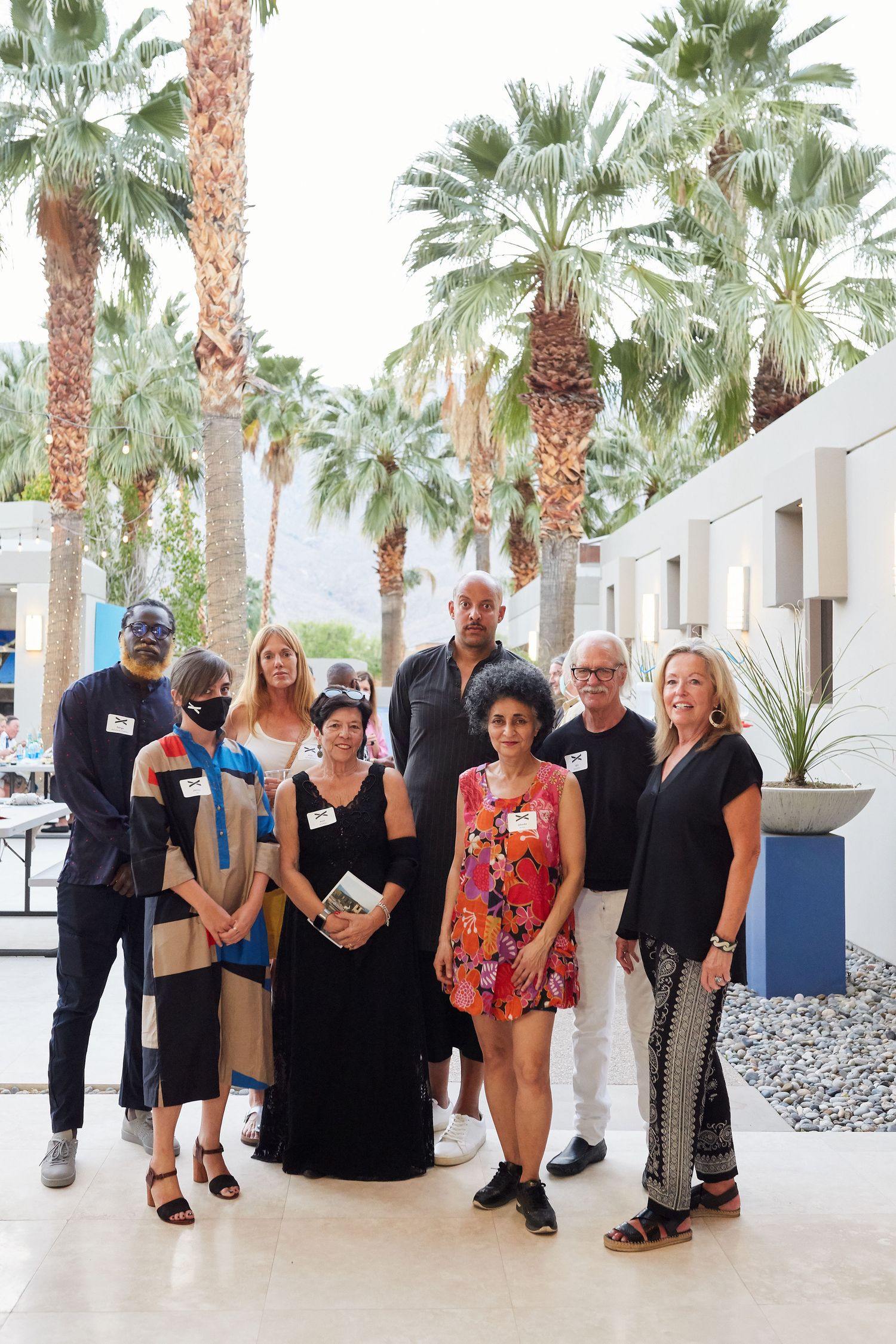 A group of professionals stand in front of palm trees and a modern building exterior in a warm desert setting.