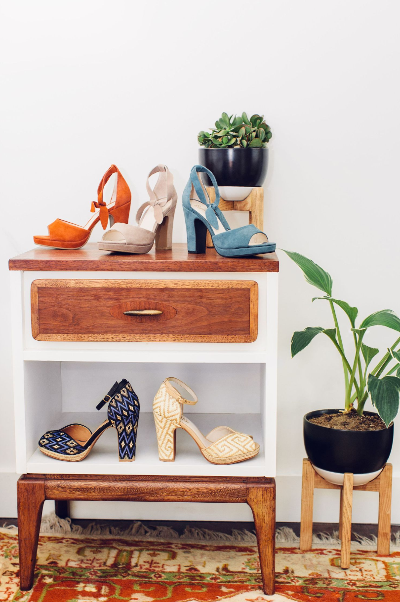 Mid-century modern side table displaying colorful women's heels and potted plants.