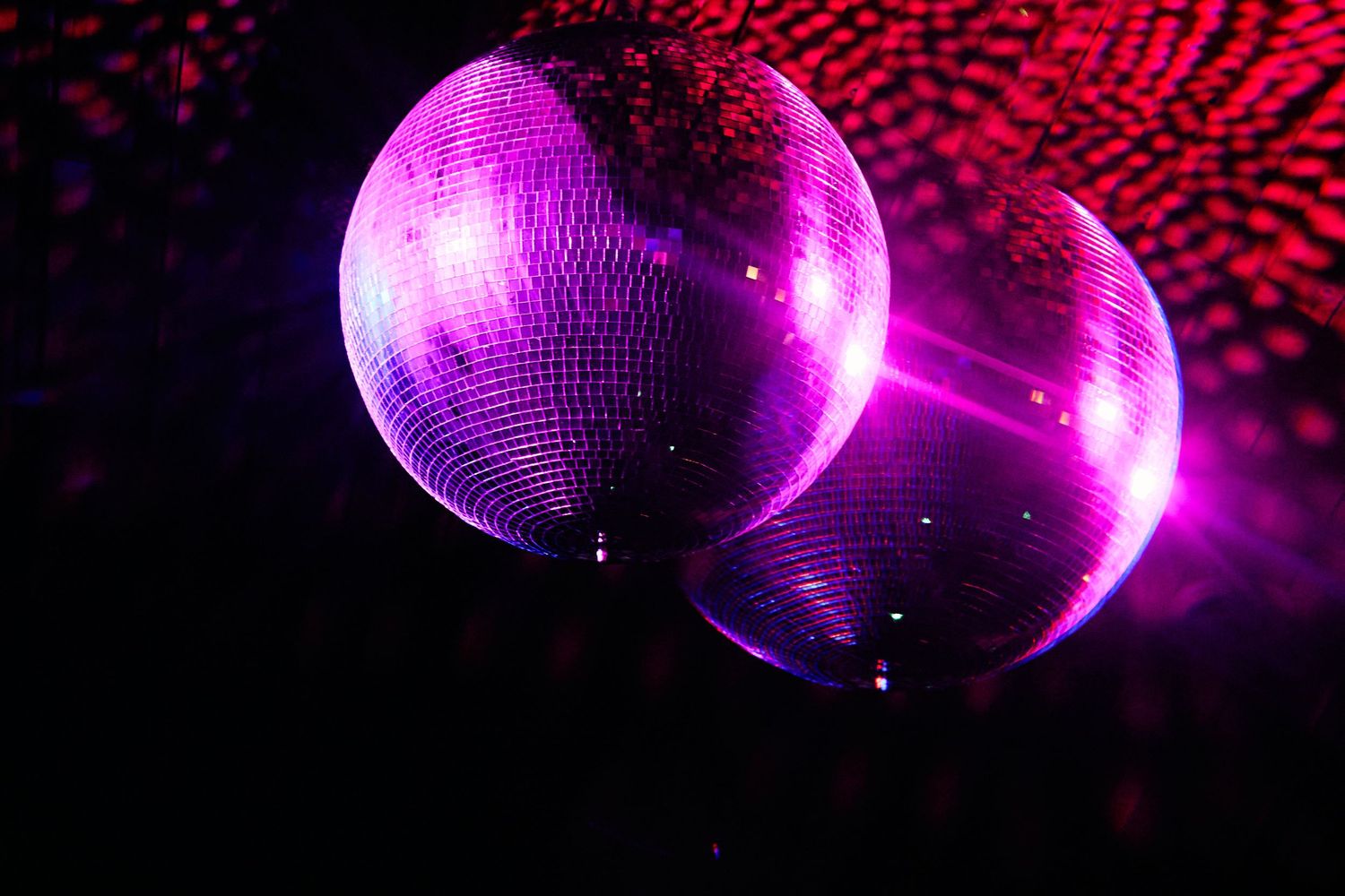 Two illuminated purple disco balls reflecting light in a dark room with red accents.