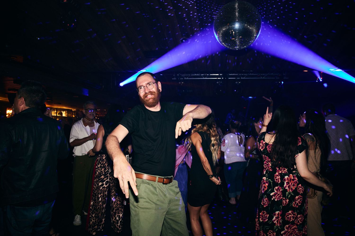 Silhouettes of people dancing and moving on a nightclub dance floor illuminated by purple lighting.