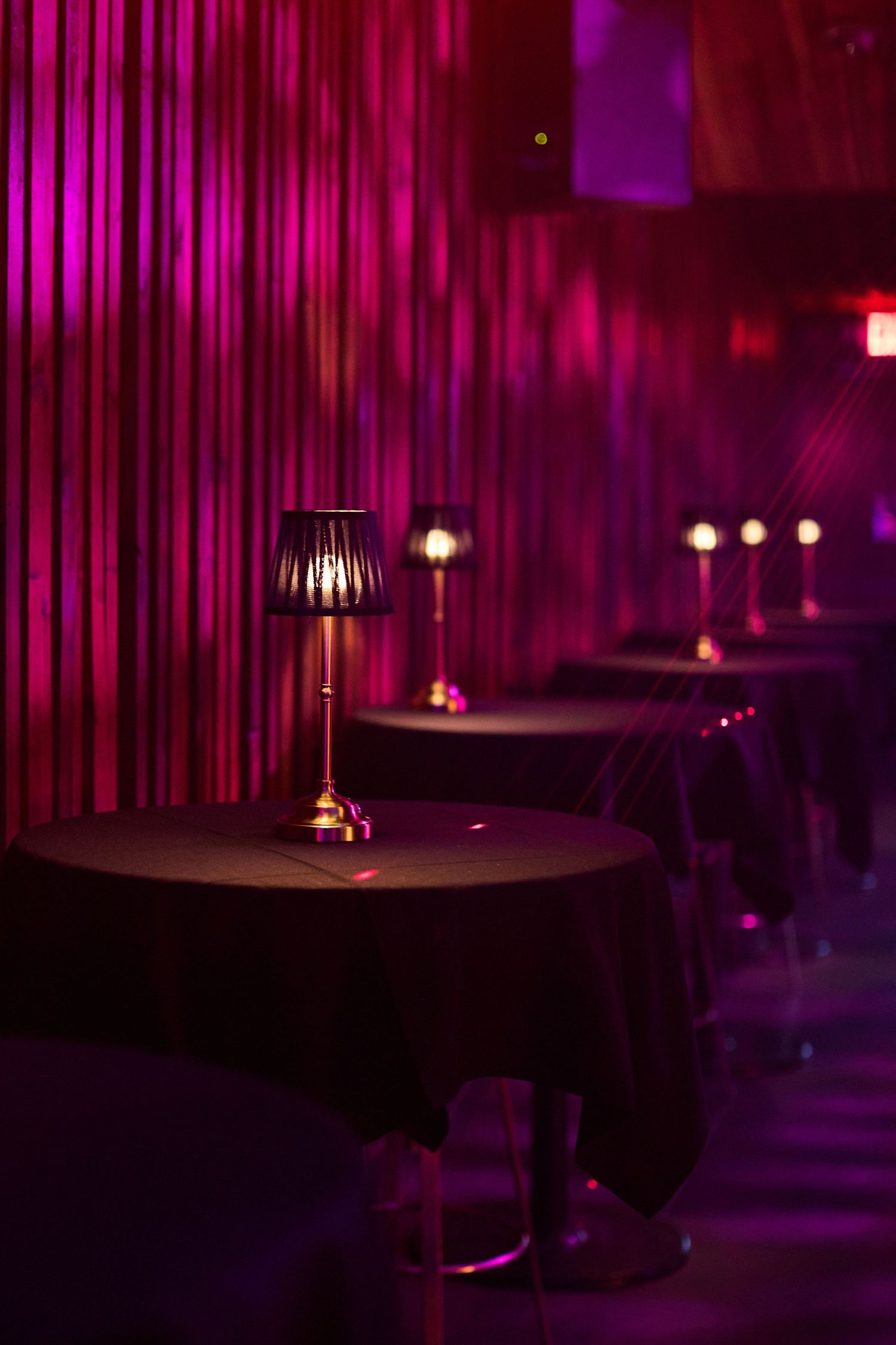 A moody lounge interior with deep magenta lighting, vertical curtains, and ambient lantern decorations creating atmosphere.
