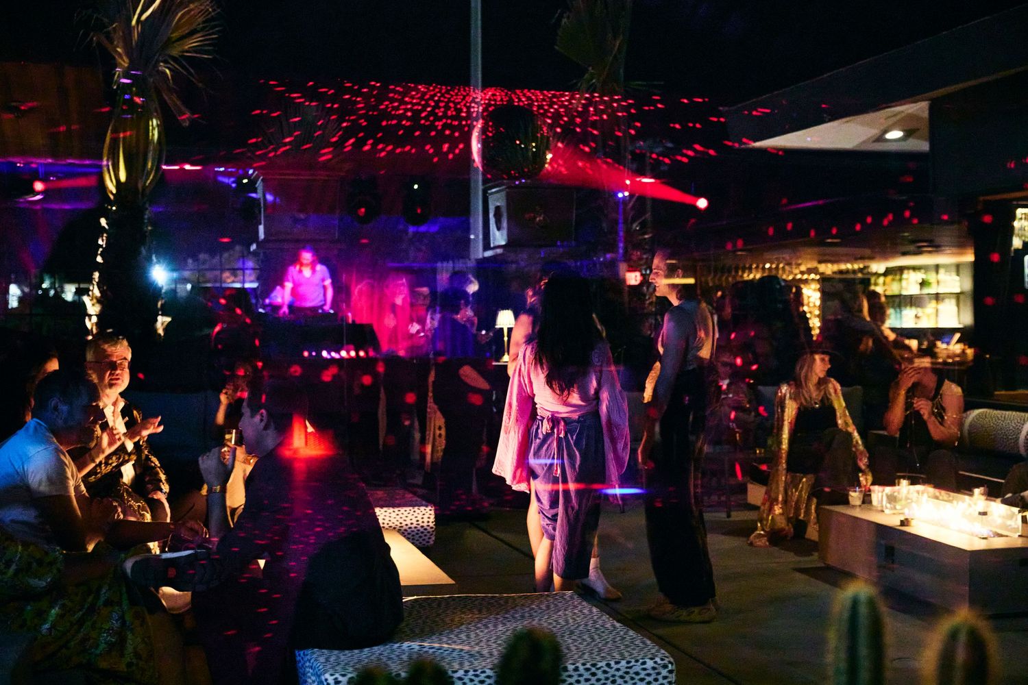 Nightclub dance floor illuminated with pink and purple lights while people dance and socialize.