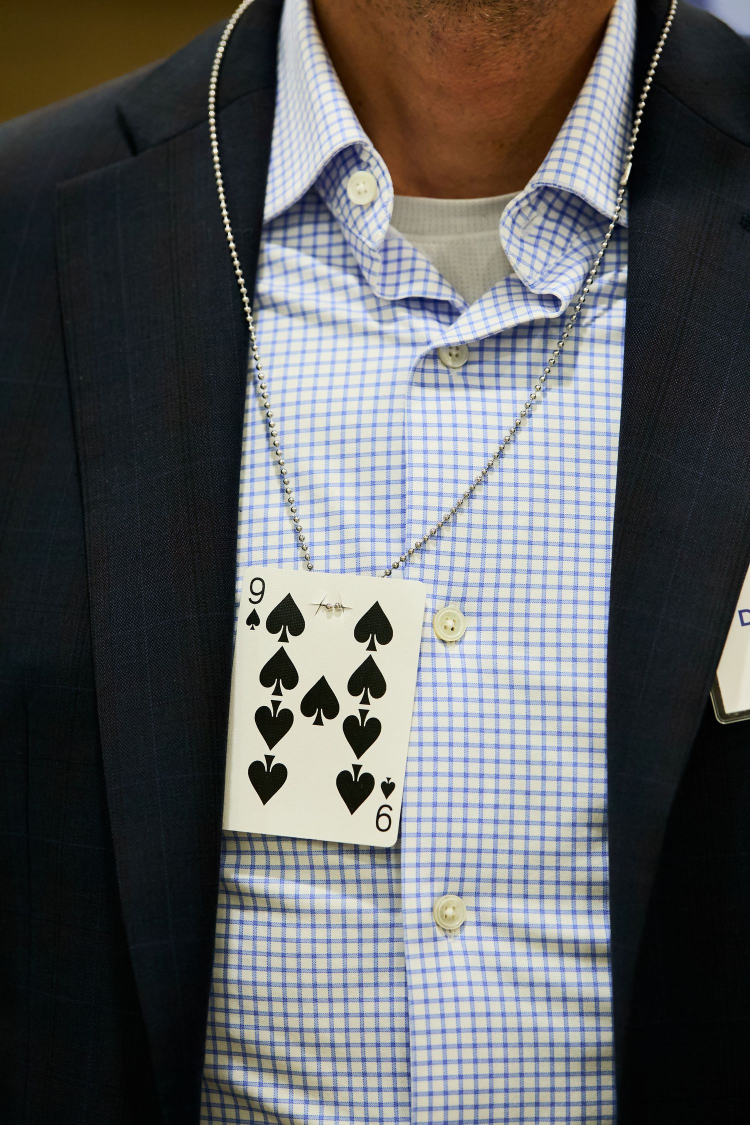 Playing card necklace featuring the nine of spades worn with a checkered blue shirt and dark blazer.