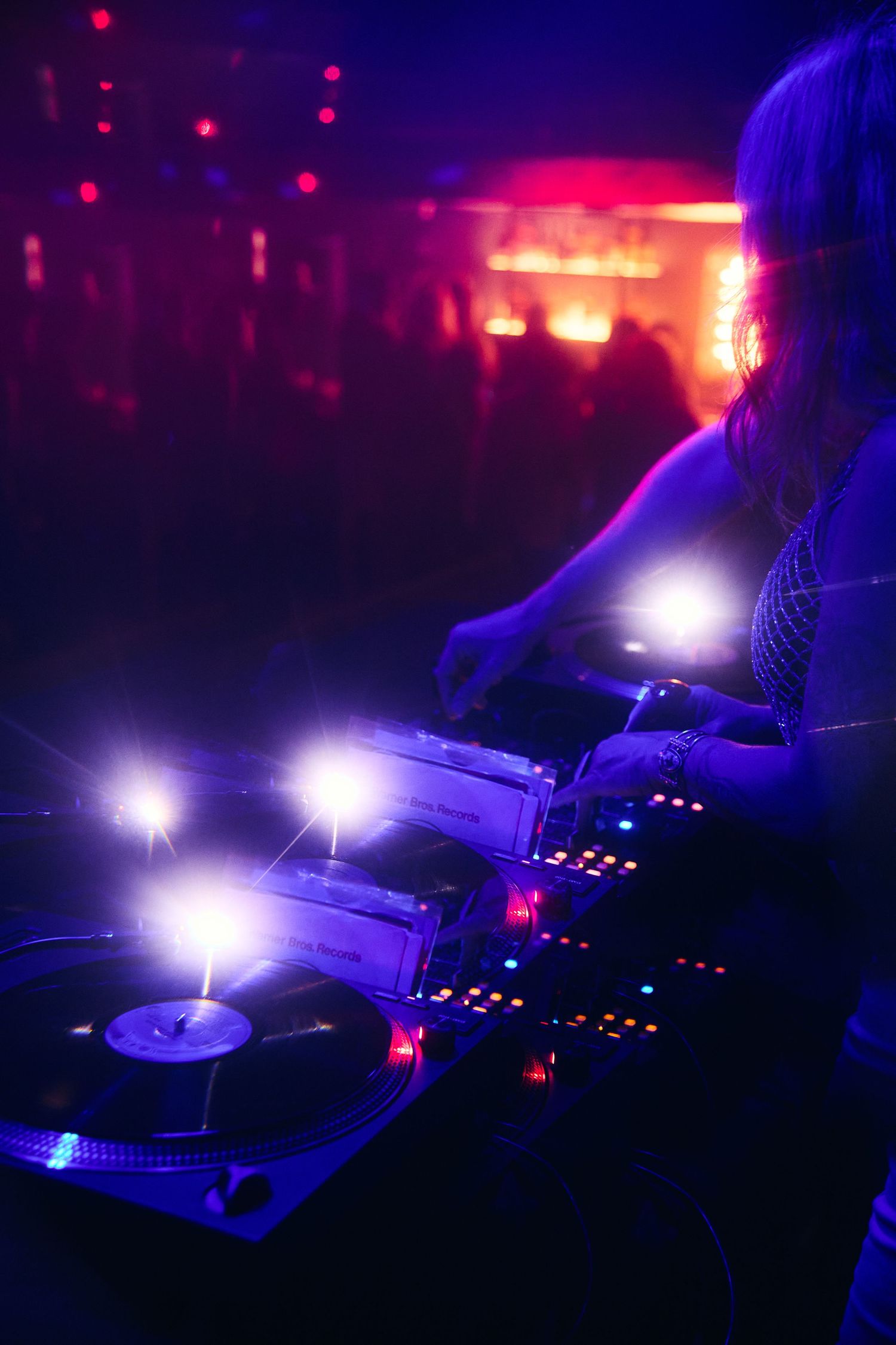 A DJ performs at a nightclub with turntables illuminated by purple and red lighting while mixing music.
