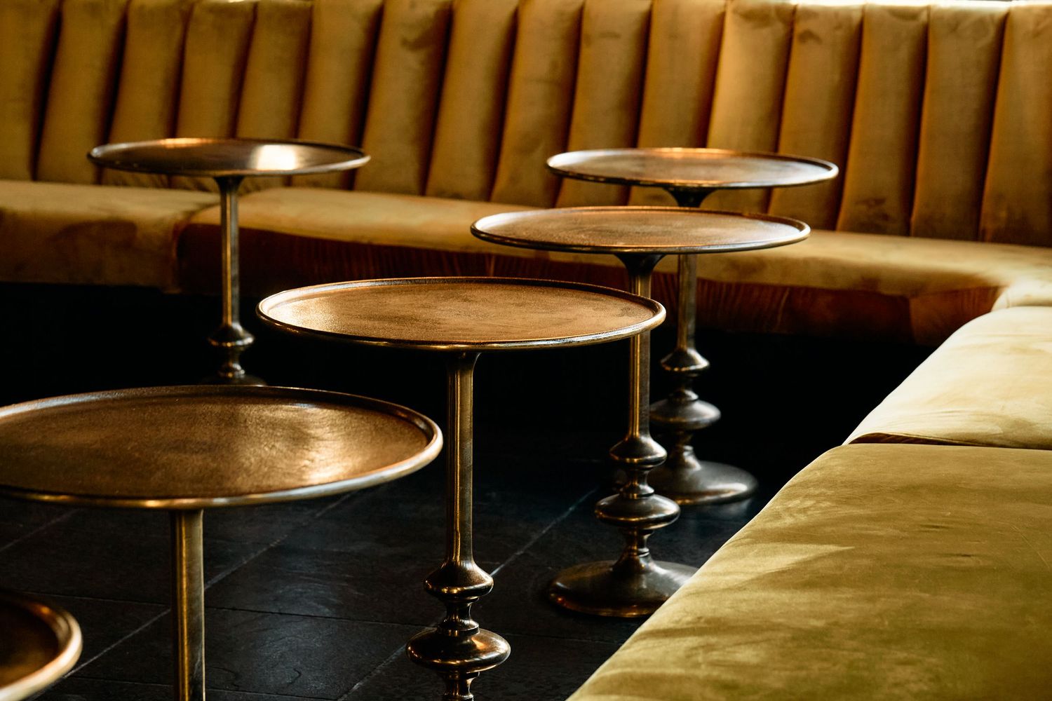 Sleek circular brass tables line up against brown leather banquette seating in an upscale restaurant interior.