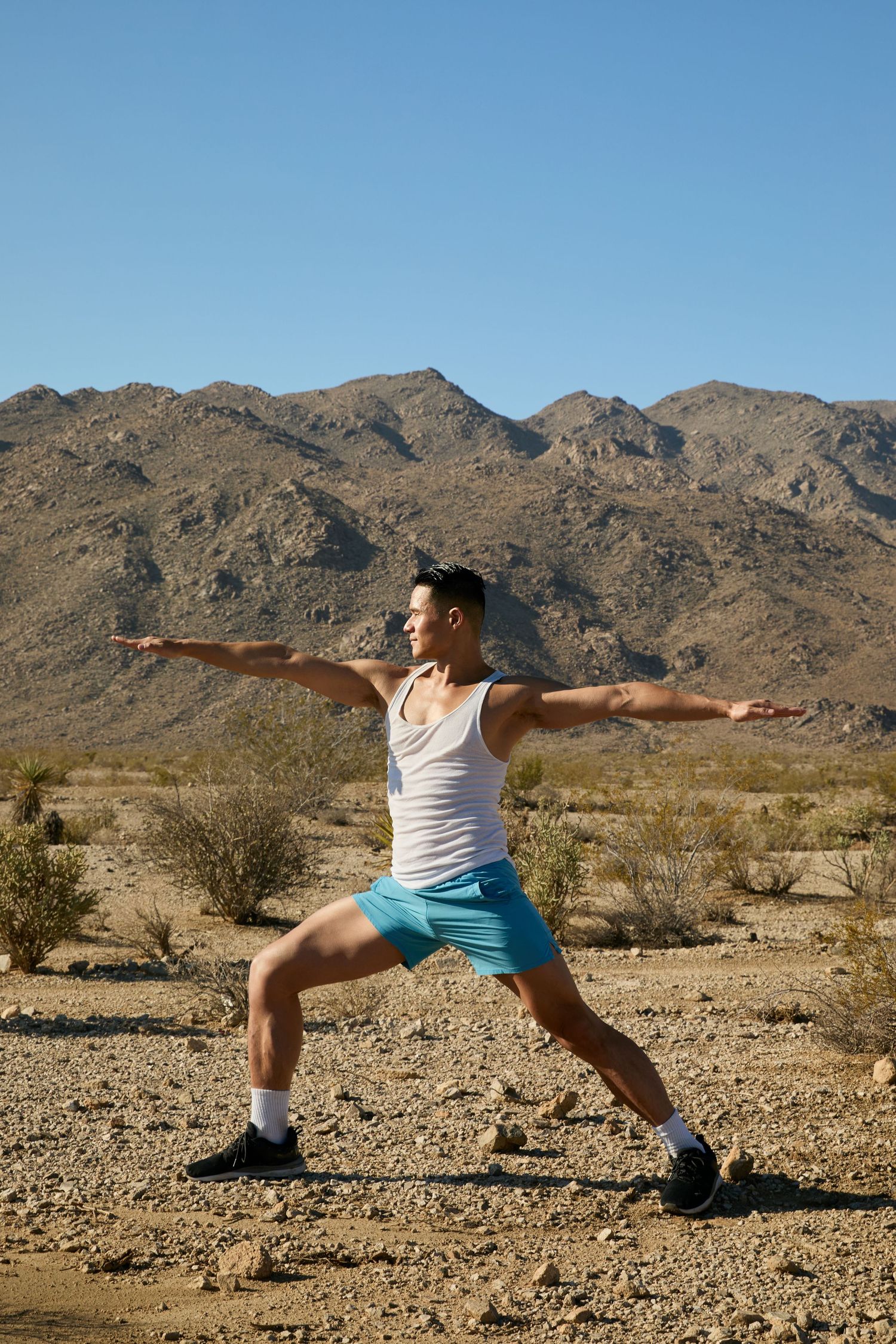 Person in white tank top and blue shorts performs dynamic lunges against desert mountain backdrop in sequence.