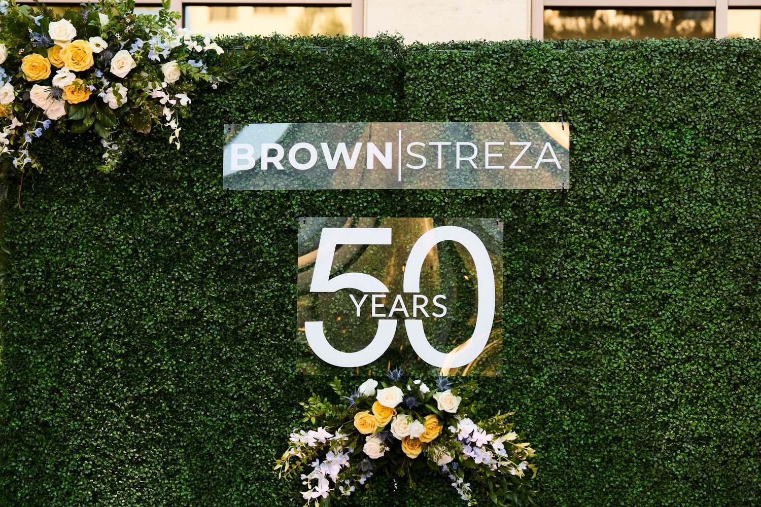 A decorative green hedge wall with gold and white balloons and the number 50 displayed for an anniversary celebration.