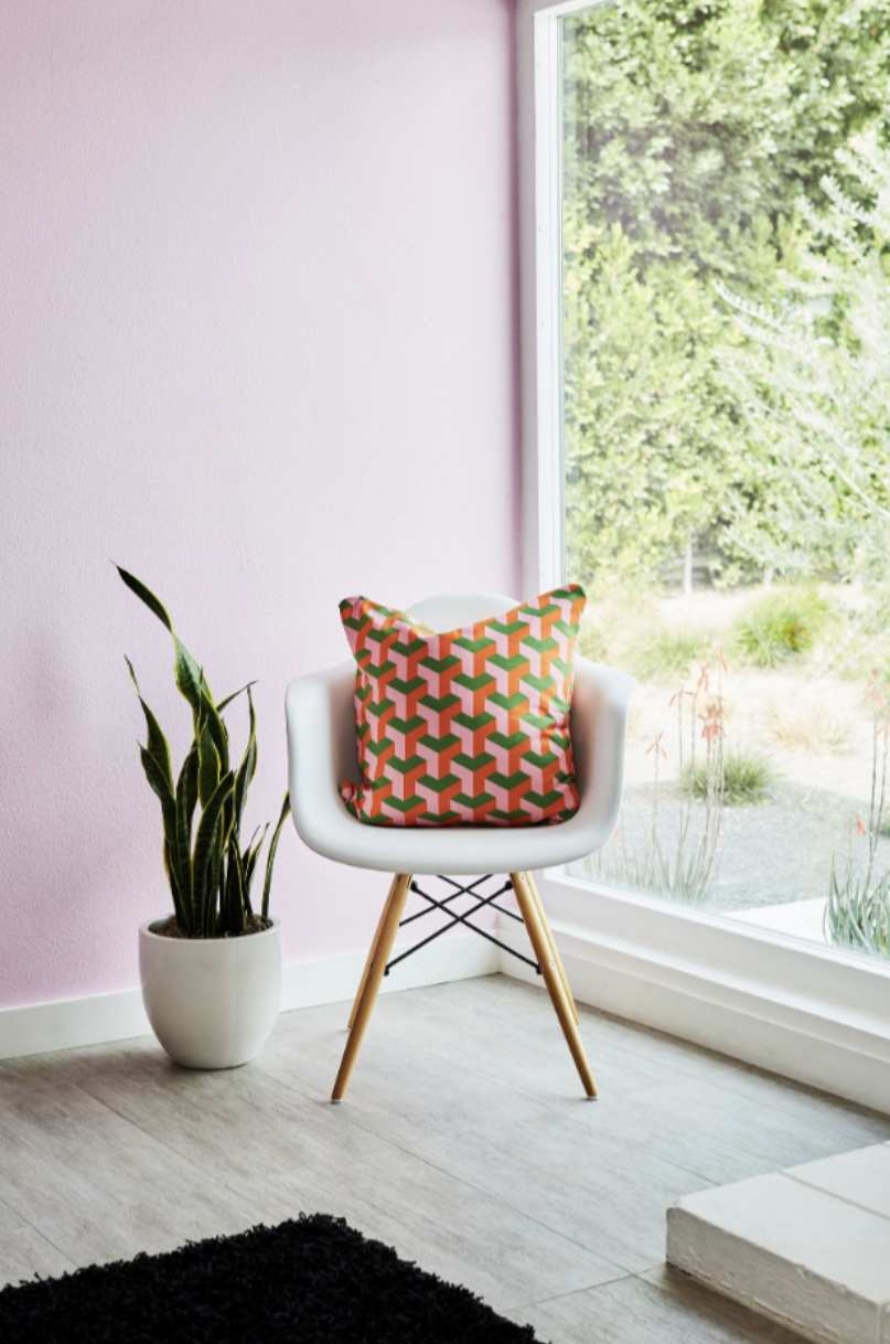 Minimalist white chair with geometric patterned pillow next to potted plant by bright window.