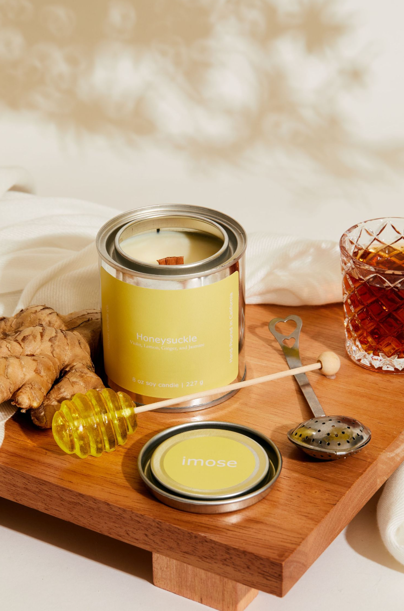 Wooden serving board with yellow candle tin, honey dipper, and cocktail glass in elegant setup.